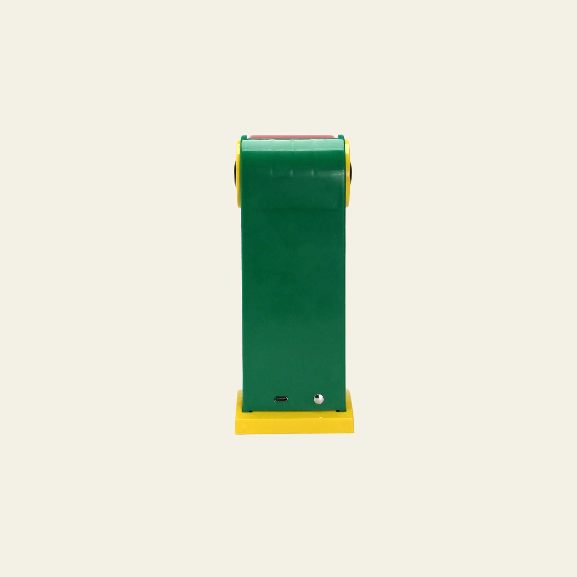 The DETAIL Toucan Lamp by DETAIL stands upright against a beige background, showcasing its green rectangular body, yellow base, and yellow accents. Its playful retro design exudes vintage charm in this rear view.
