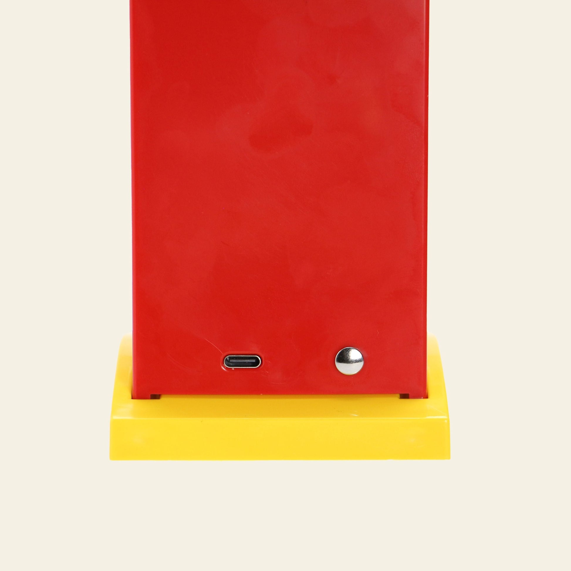 A close-up of the bottom of the red DETAIL Toucan Lamp by DETAIL, featuring a USB-C port and round metal button on a yellow base against a beige background, showcasing its vintage charm.