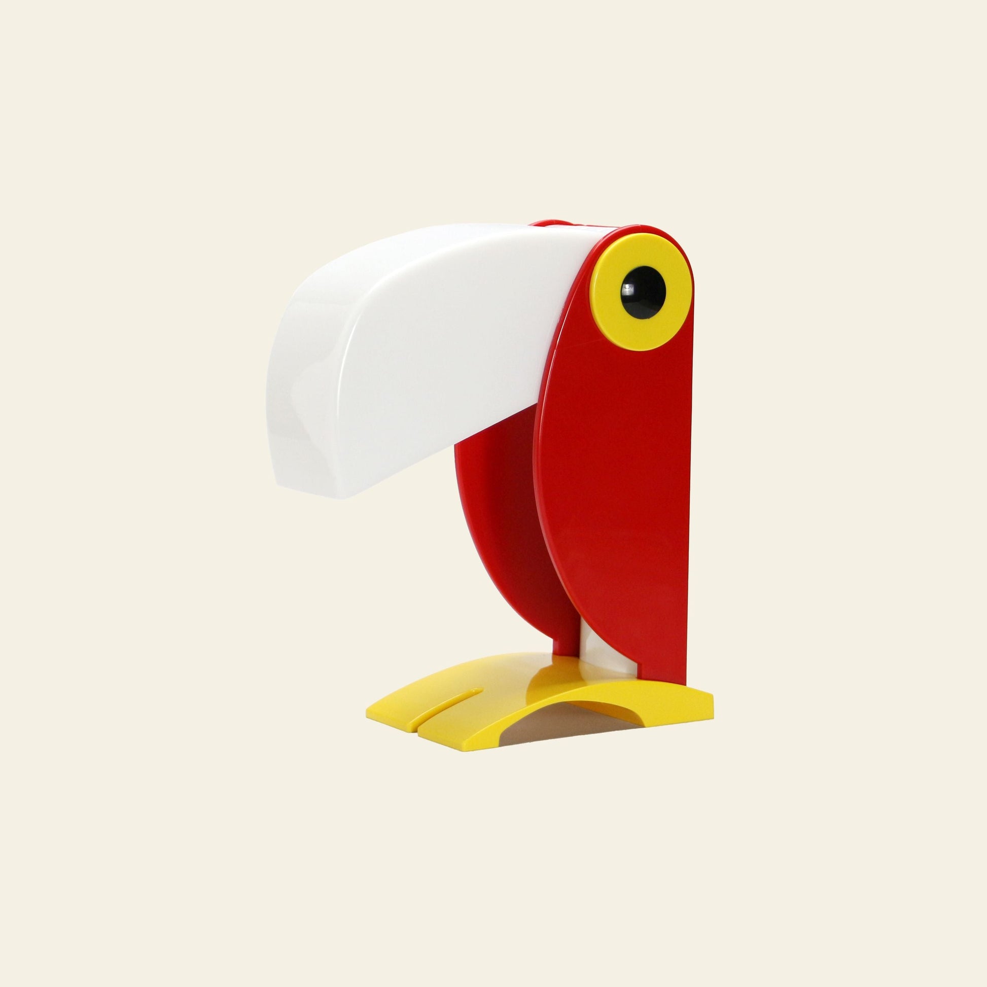 The DETAIL Toucan Lamp by DETAIL features a large white beak-shaped lampshade and vibrant colors, bringing iconic vintage charm to any space with its toucan-inspired design. Perfect as a statement piece against neutral backgrounds.