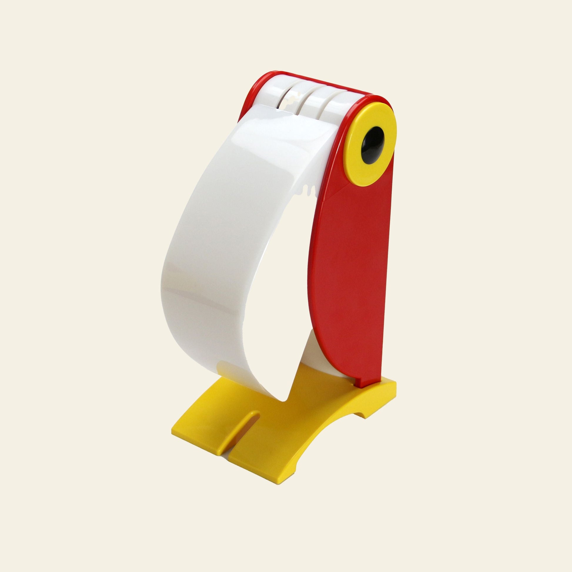 The DETAIL Toucan Lamp by DETAIL, featuring its iconic design in red, yellow, and white, stands upright on a light beige background.
