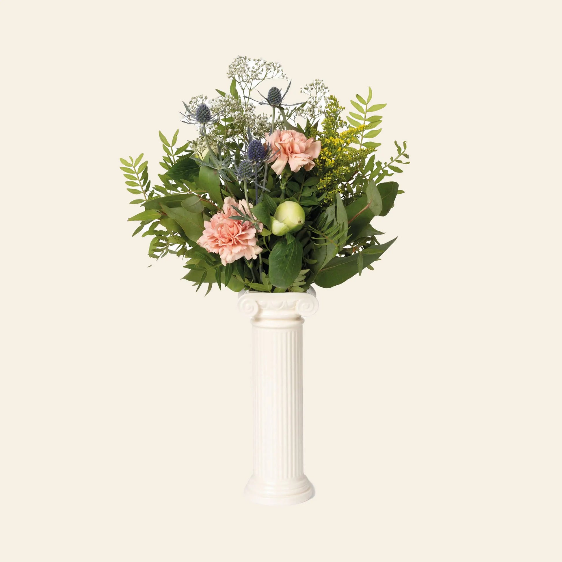 The DOIY Athena Vase by DOIY, inspired by a Greek Ionic column, displays pink carnations, green foliage, blue thistles, and yellow flowers against a plain beige background.