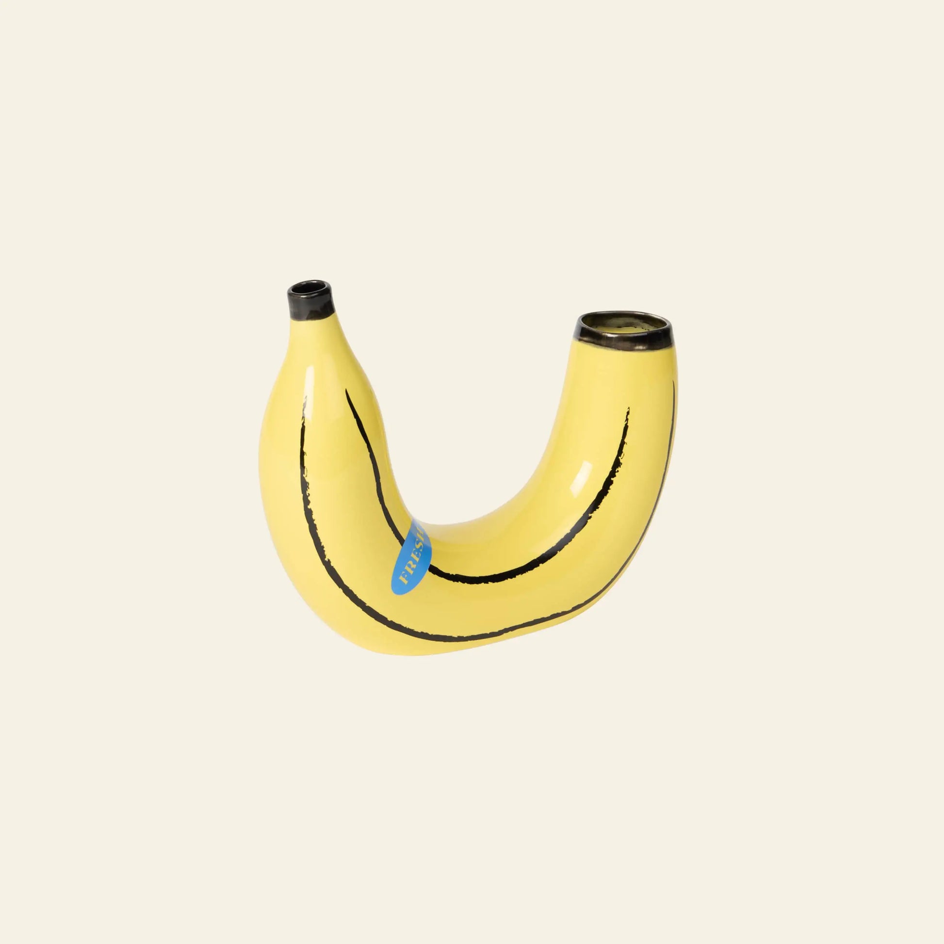 The DOIY Banana Vase by DOIY is a playful, curved yellow vessel with two open ends and a blue sticker accent—an eye-catching home decor piece that adds fun to any space.