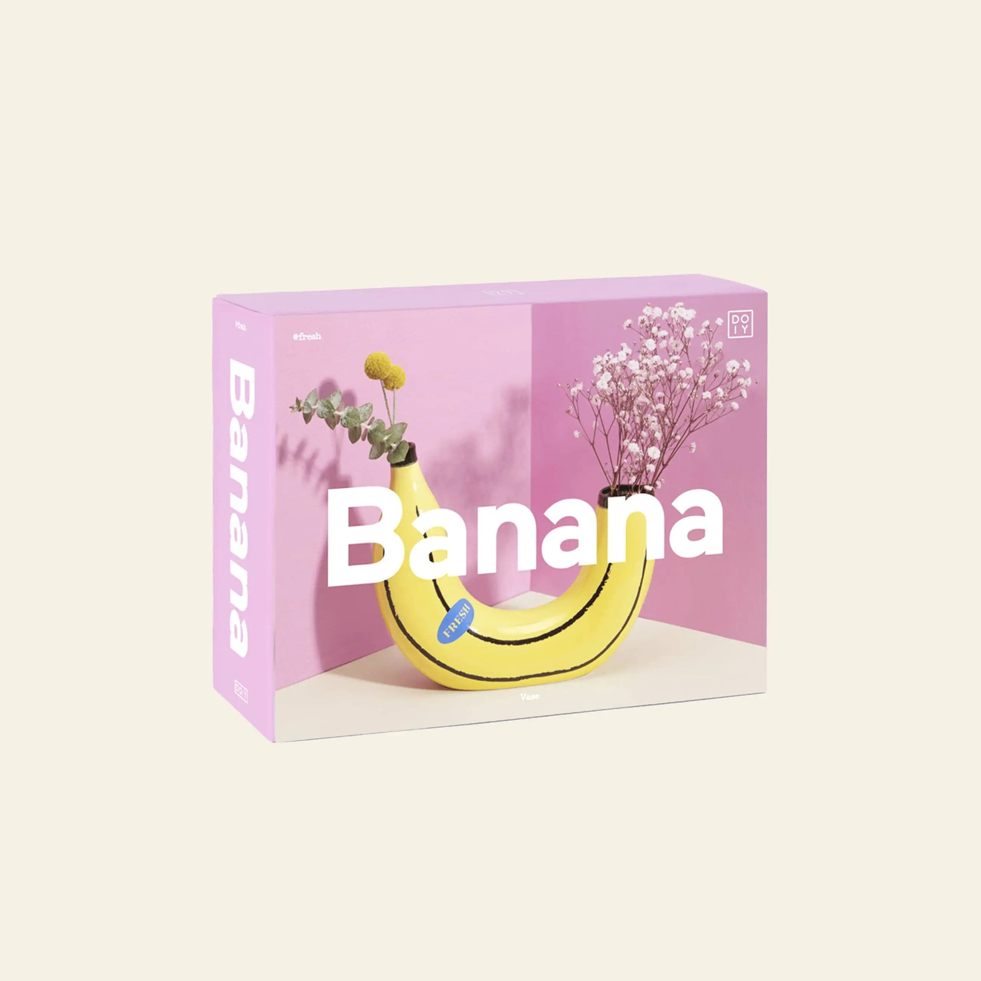The DOIY Banana Vase by DOIY features a playful banana-shaped vase holding flowers, ideal for home decor. The product box displays Banana across the front, set against a pink and beige background for added charm.