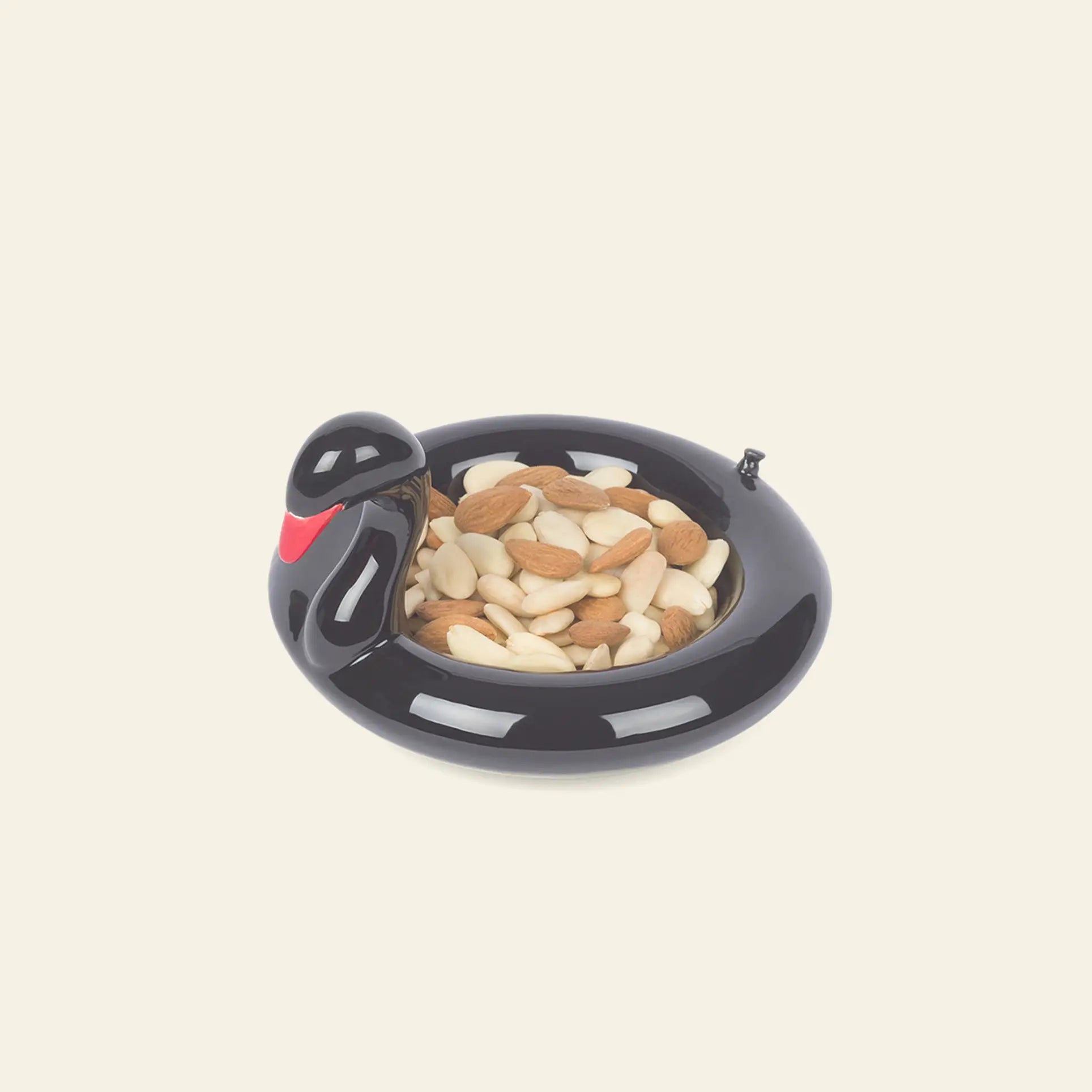 The DOIY Black Swan Floatie Bowl by DOIY, a black, glossy ceramic bowl shaped like a bird with a red beak, serves as a charming decorative accent filled with mixed nuts against a plain beige background.