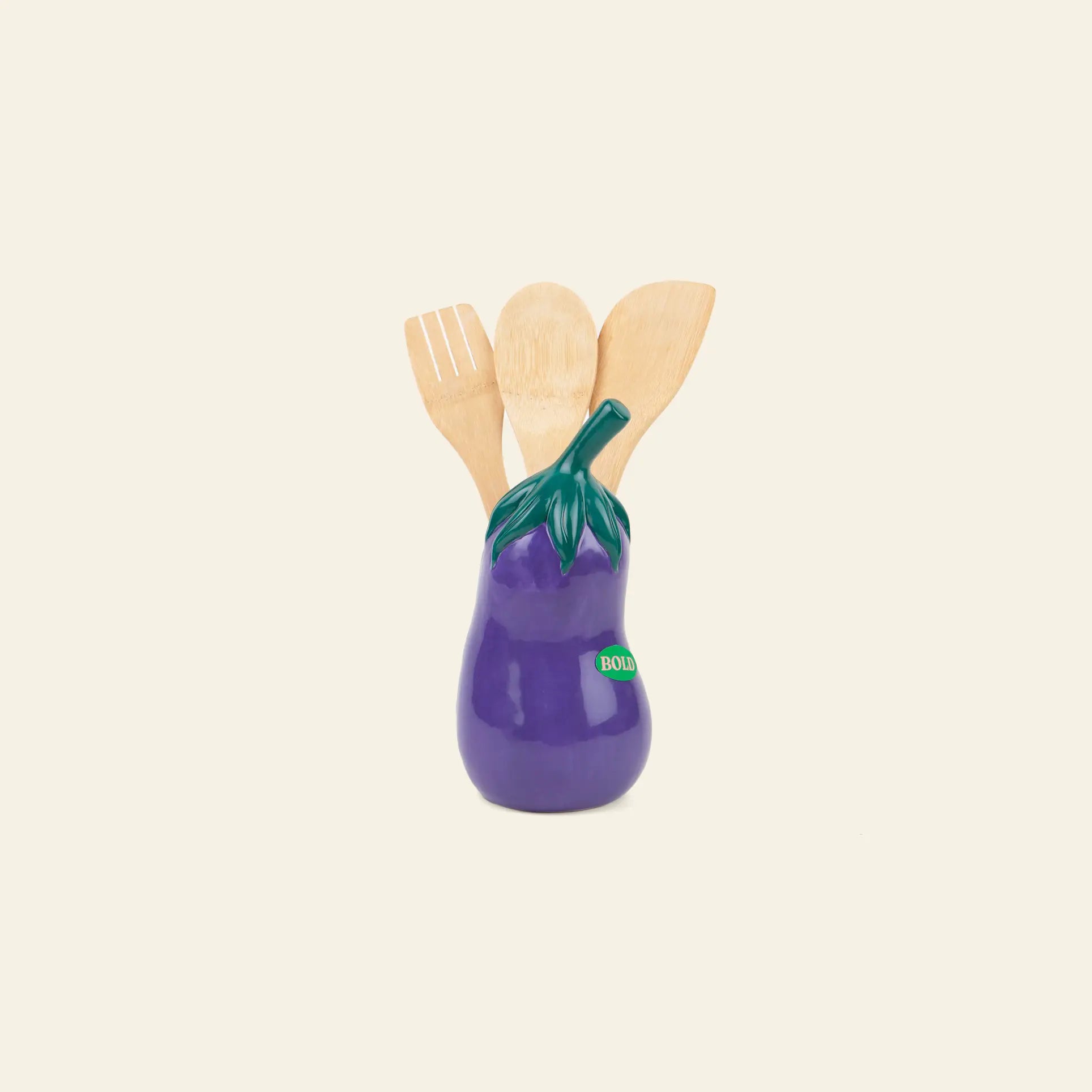 The DOIY Farmers’ Market Eggplant Utensils Pot by DOIY holds three wooden kitchen essentials—spoon and spatulas—bringing playful vegetable-themed decor to your countertop against a plain light background.