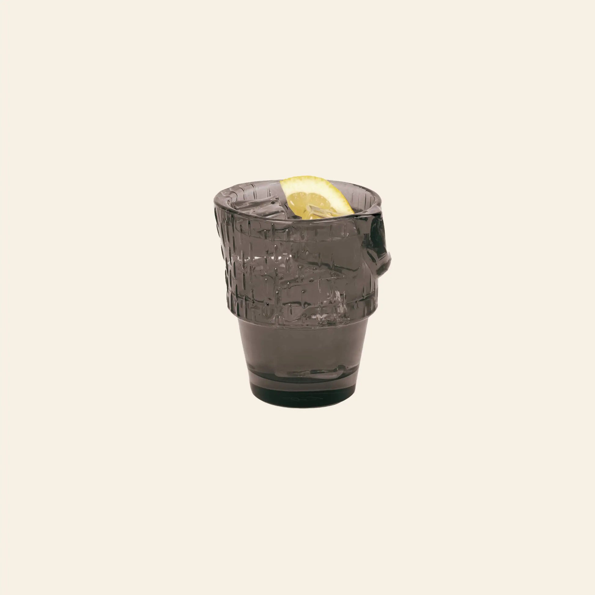 A stackable, dark DOIY Kitty Glass from the DOIY Kitty Glasses Set of 4, filled and garnished with a lemon wedge, stands out against a plain light beige background.