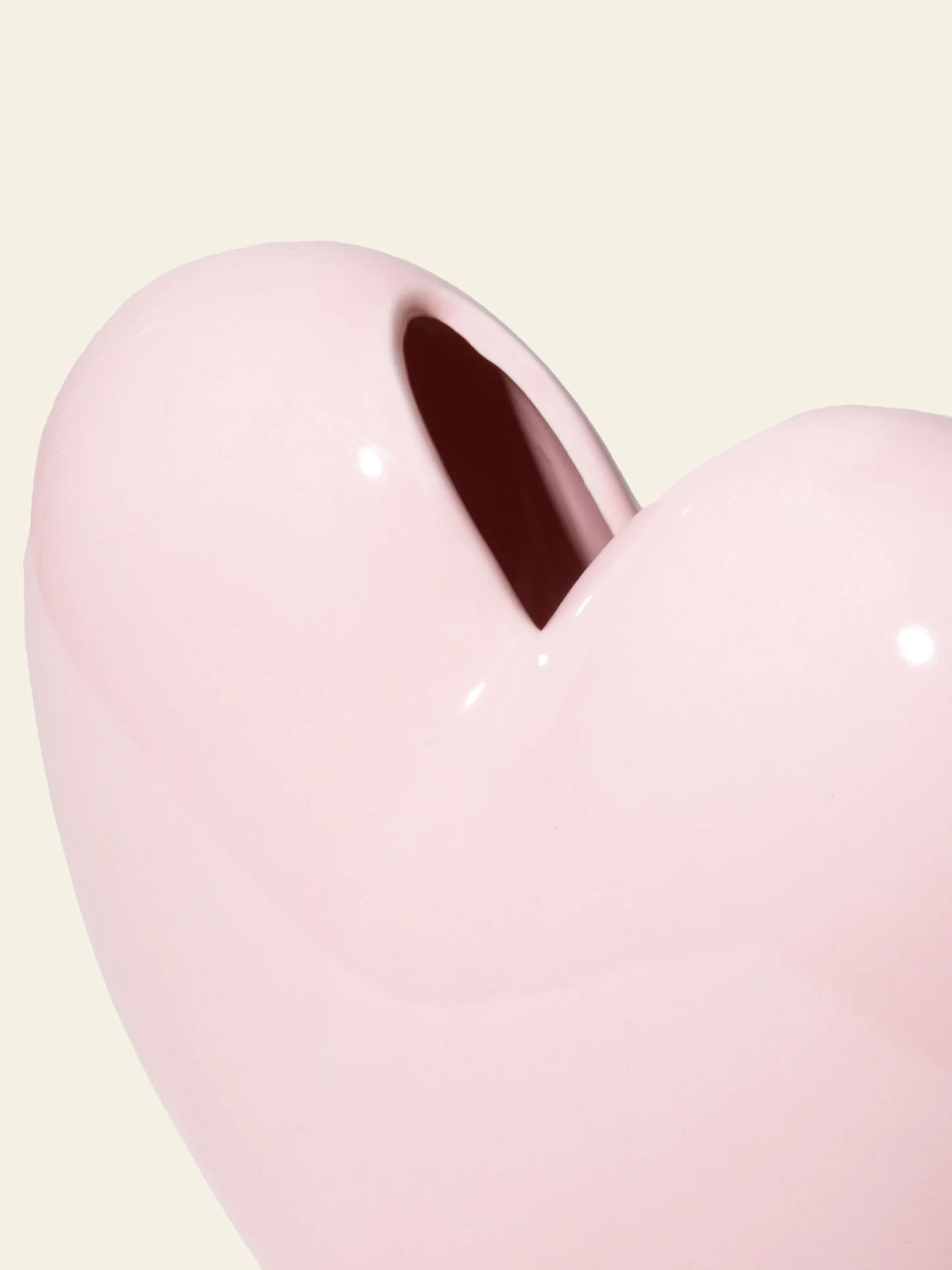 Close-up of the DOIY Love Vase by DOIY, a shiny, light pink heart-shaped vase with a top opening, set against an off-white background. This elegant piece brings sentimental charm and timeless beauty to any space.
