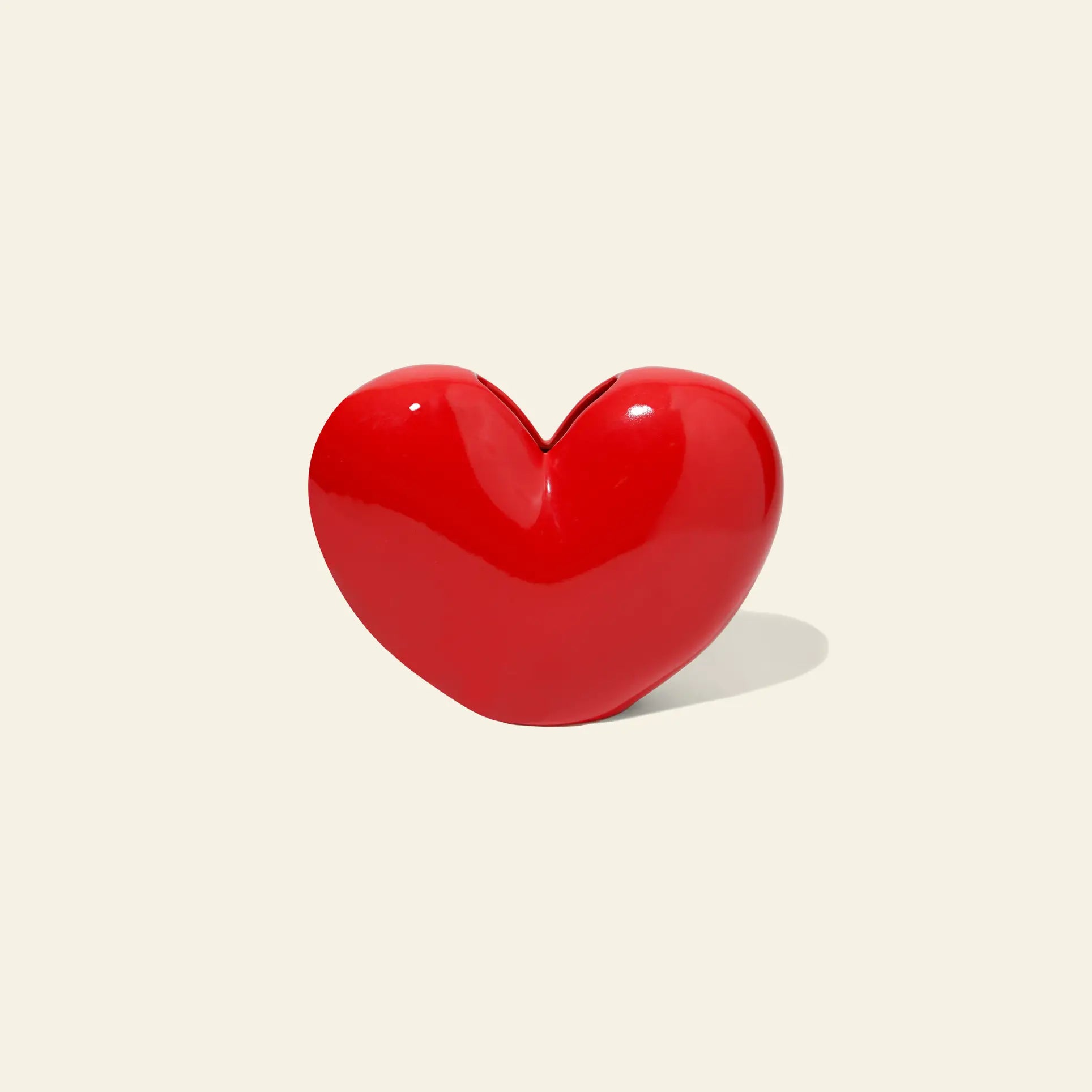 The DOIY Love Vase by DOIY stands upright on a light beige background, its shiny red heart-shaped design casting a subtle shadow to the right and exuding timeless beauty.