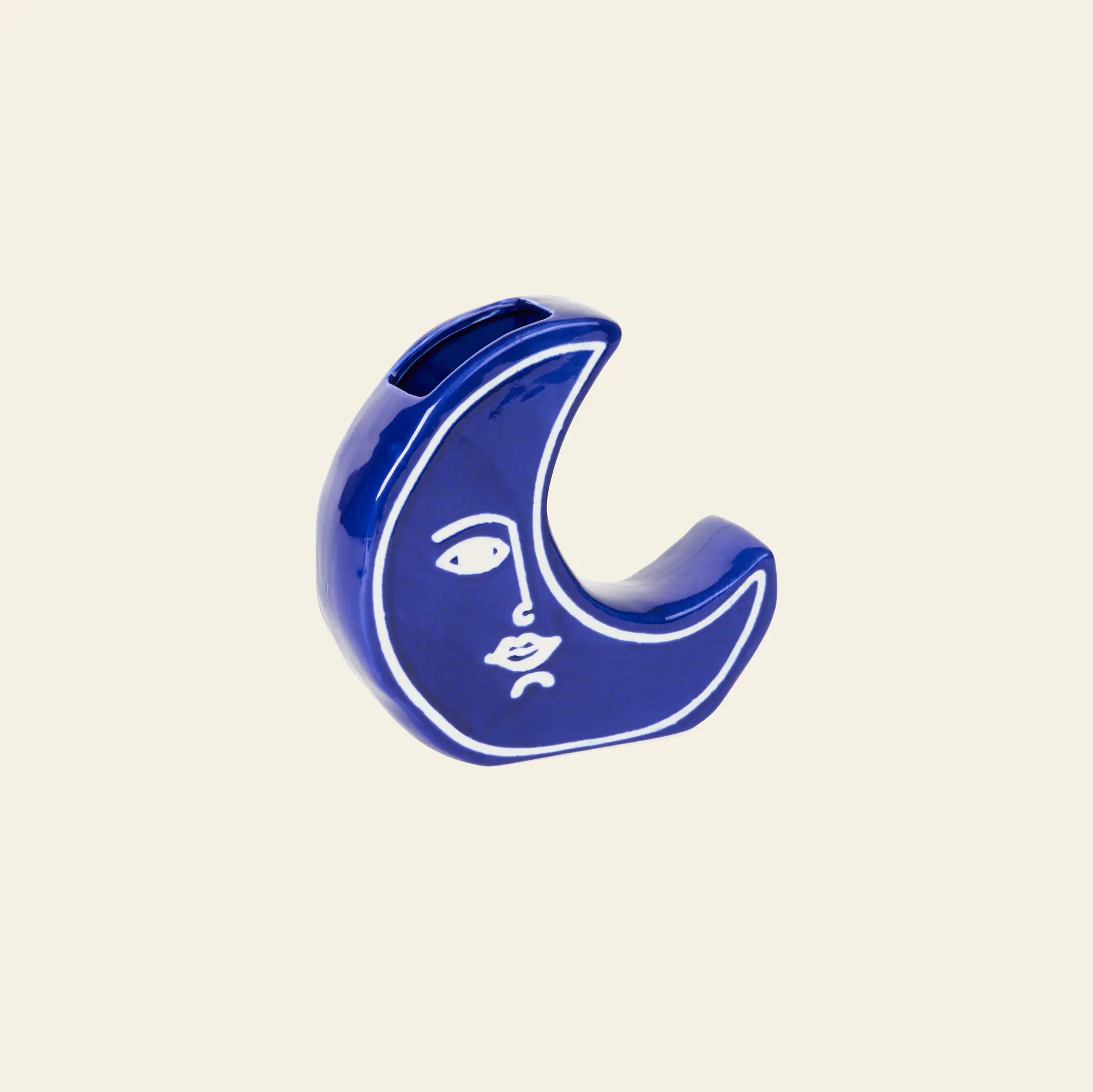 The DOIY Moon Vase by DOIY is a blue crescent-shaped ceramic vase, featuring a minimalist white line face design, shown against a plain beige background.
