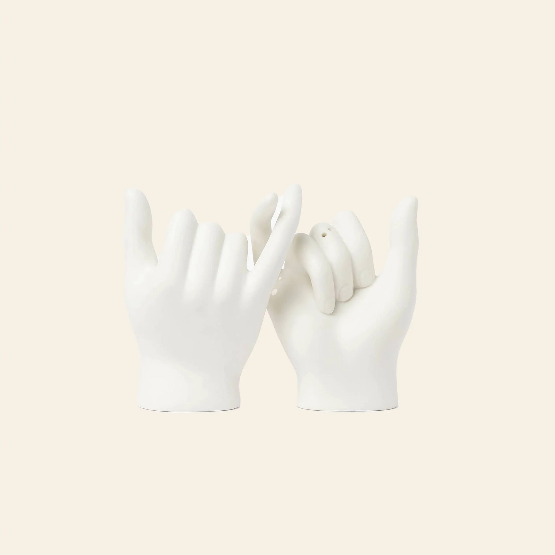 The DOIY Pinky Swear Salt and Pepper Set by DOIY features two white ceramic hand sculptures with interlocked pinky fingers, creating an artistic centerpiece against a light beige background.