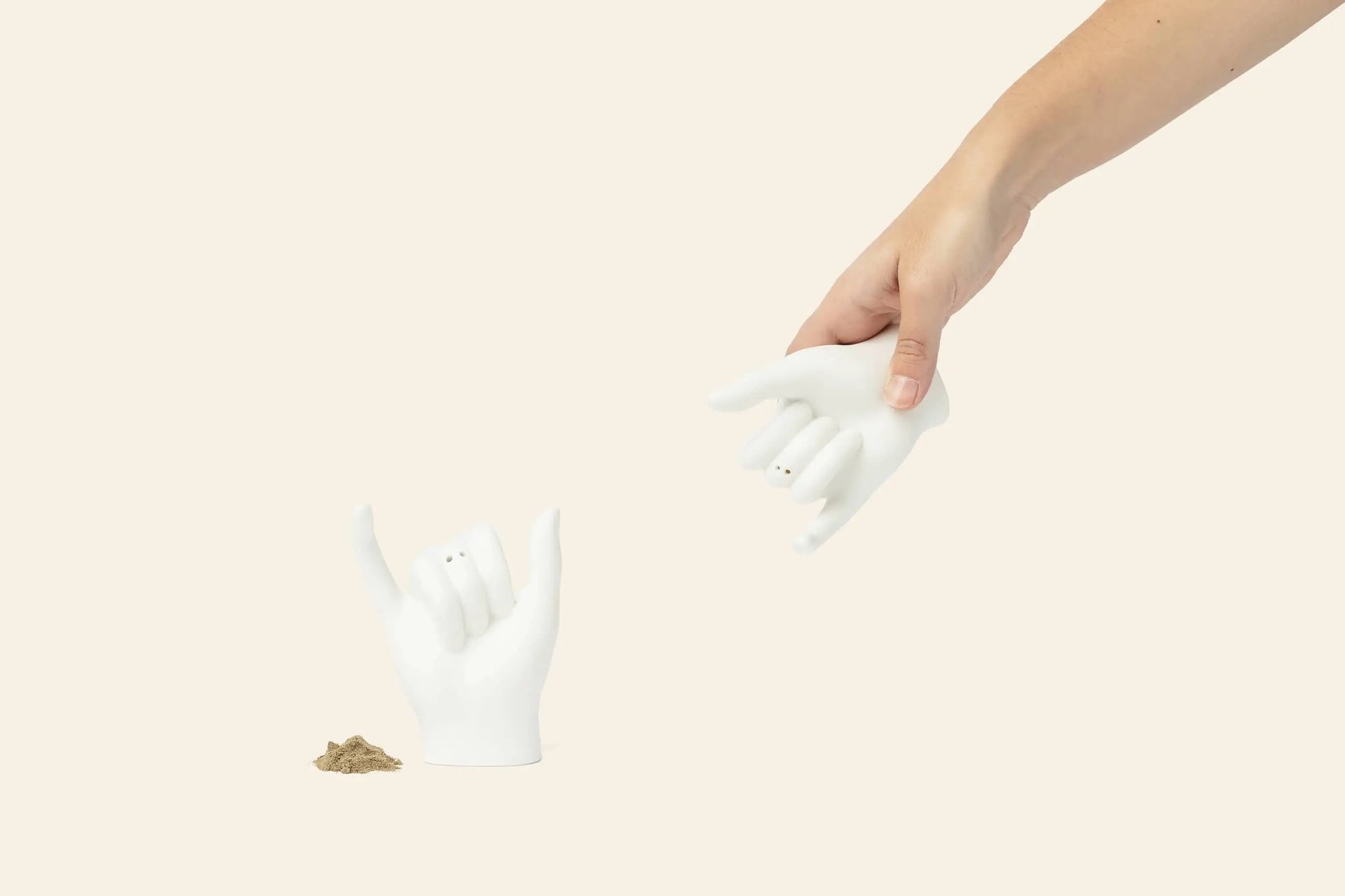 A hand holds the DOIY Pinky Swear Salt and Pepper Set—a pair of white ceramic shakers shaped like hands. This unique set by DOIY brings contemporary flair and playful artistry to your table, reinventing the classic salt and pepper duo.