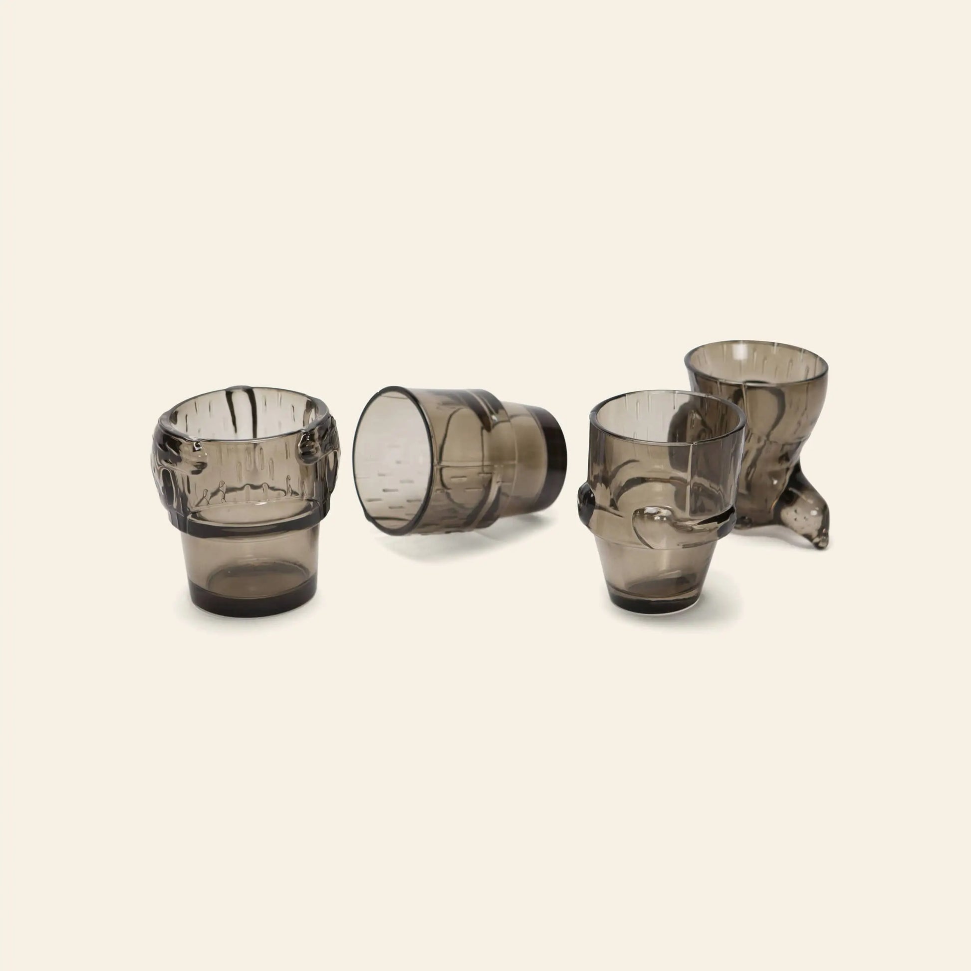 The DOIY Puppy Glasses Set of 4 by DOIY features uniquely shaped, smoky gray glasses with distinct artistic forms and textures, perfect as modern, handcrafted decorative pieces. Displayed on a light beige background.