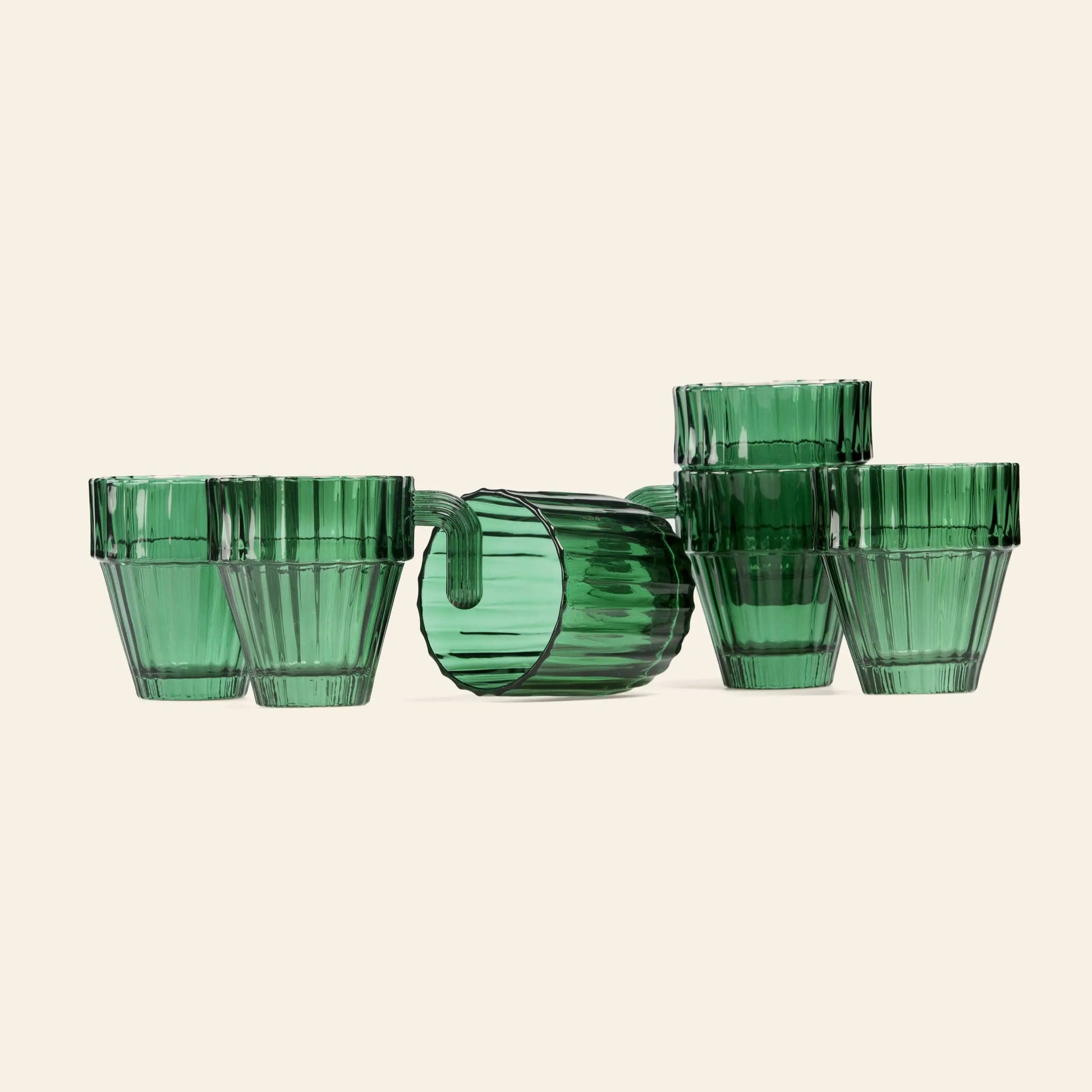 The DOIY Saguaro Glasses, Set of 6 by DOIY features green ribbed tumblers arranged with five upright in a semicircle and one on its side, creating a stylish display against a light background for modern home decor.