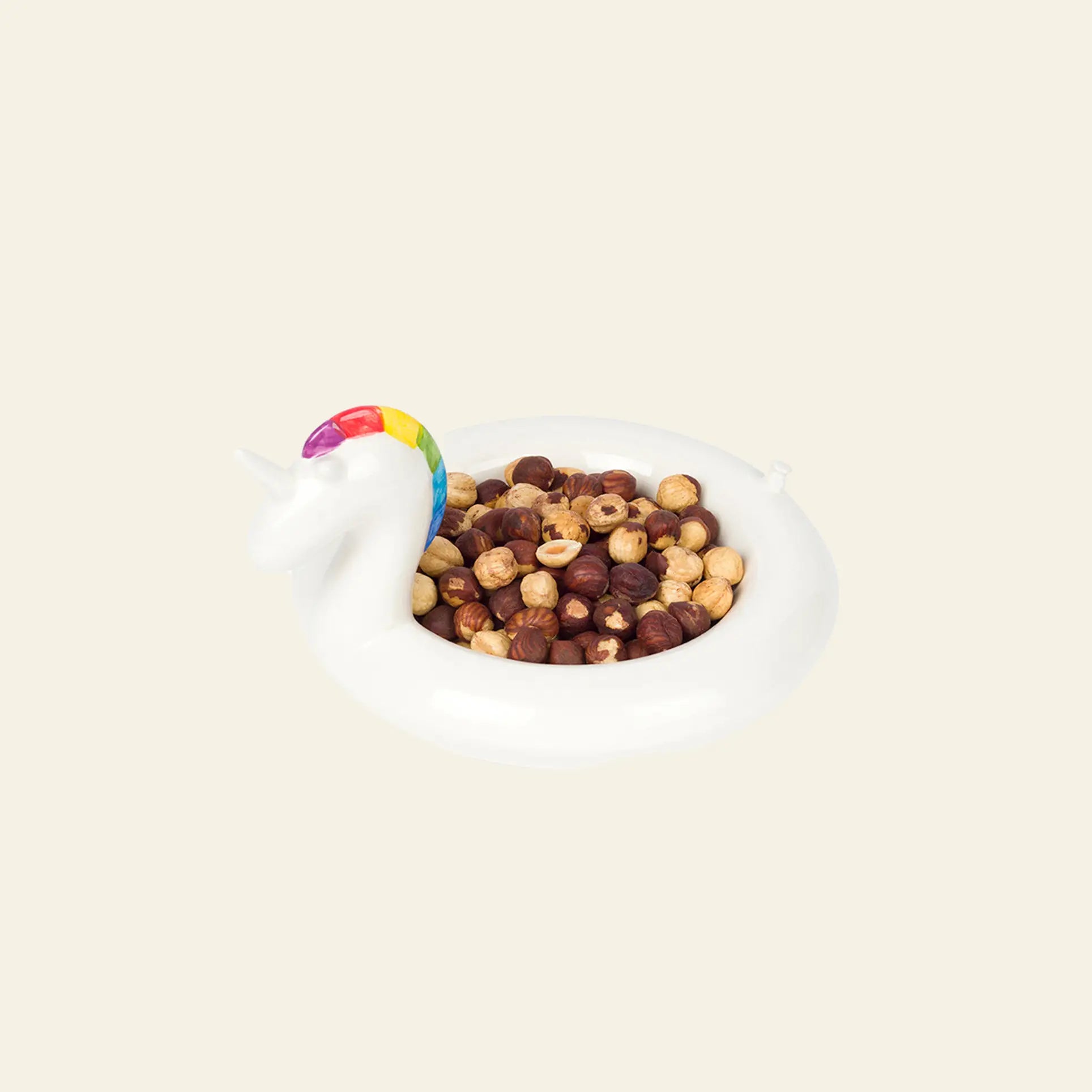 The DOIY Unicorn Floatie Bowl by DOIY, a white ceramic unicorn-shaped bowl with a rainbow mane, is filled with assorted hazelnuts and placed against a plain light background for a whimsical decorative touch.
