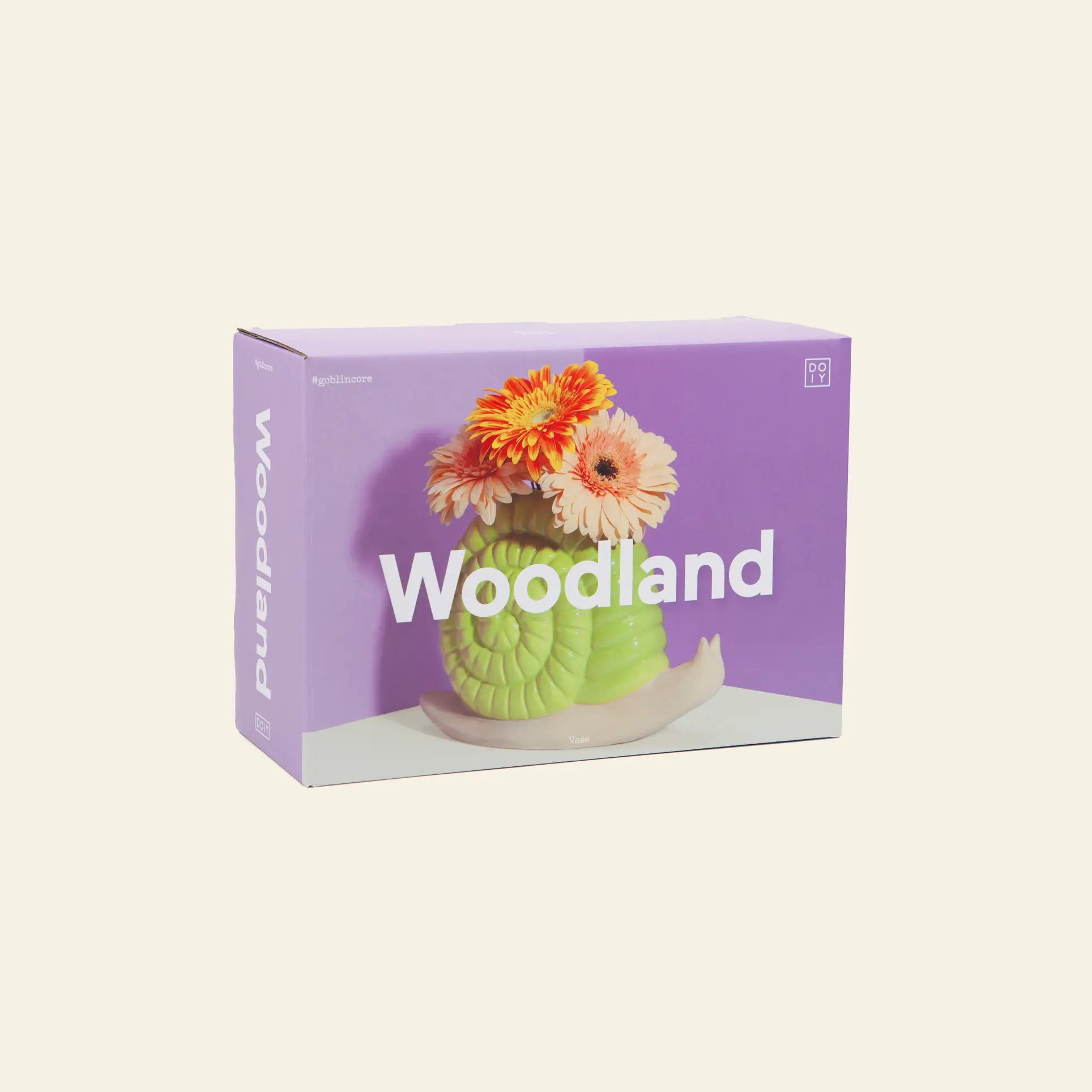 A box featuring a photo of the DOIY Woodland Snail Vase, a green snail-shaped ceramic vase by DOIY holding orange and pink flowers on a purple background. Woodland is boldly printed in white across the front, showcasing this decorative accent.