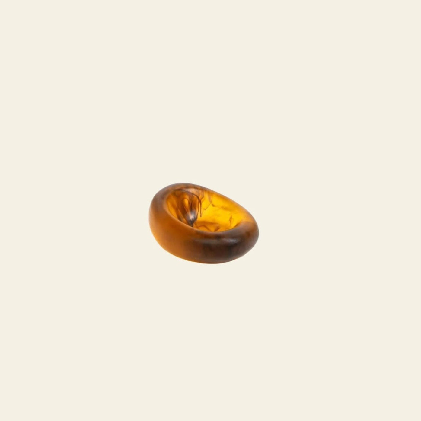 A single, smooth, oval amber gemstone with a glossy finish rests on a plain beige background, evoking the organic design of the Dinosaur Designs Small Drift Dish by Dinosaur Designs.