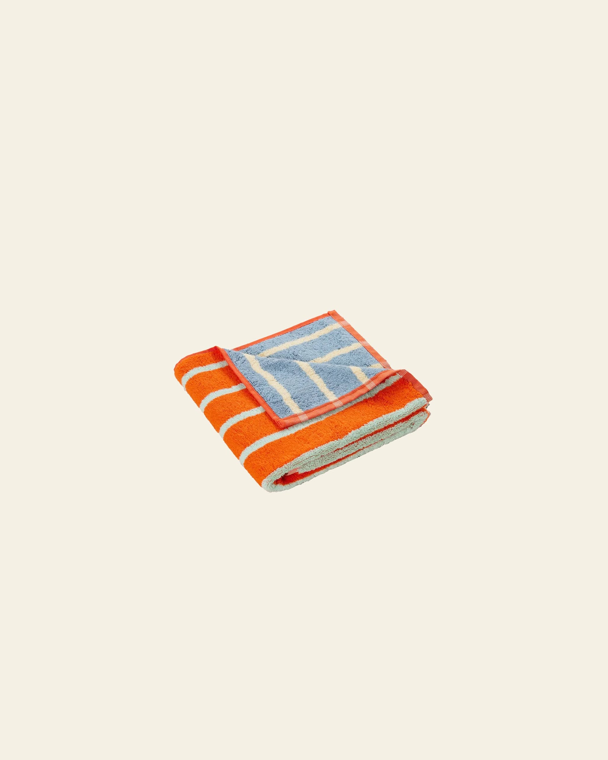 The Dusen Dusen House Stripe Stone Hand Towel—a soft towel with vibrant orange and white stripes plus blue geometric accents by Dusen Dusen—is shown on a plain beige background.