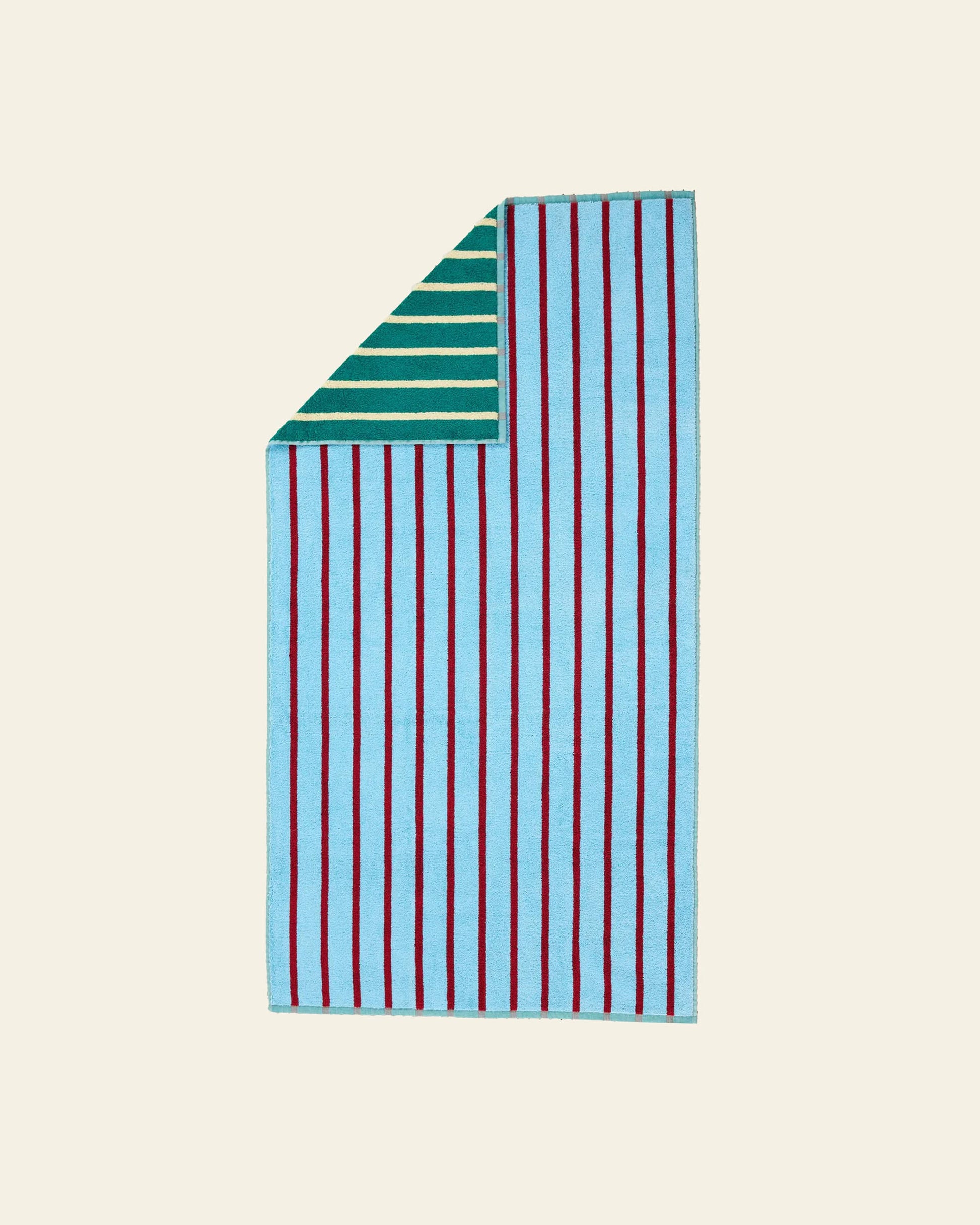 The Dusen Dusen House Stripe Tile Bath Towel by Dusen Dusen is a rectangular cotton terry towel with bold red stripes on a light blue front and vibrant green and white stripes on the reverse, shown with a folded corner against a beige background.