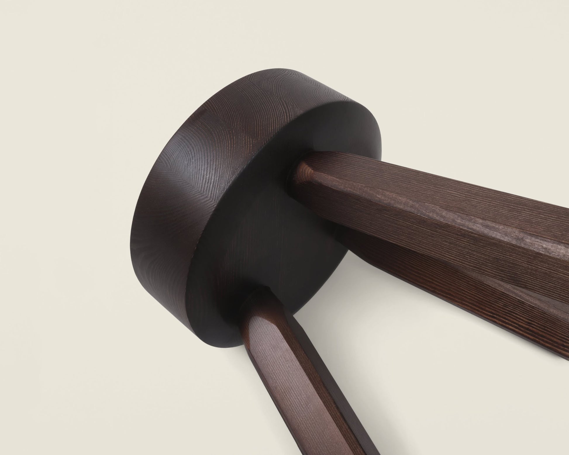 Close-up of the FRAMA AML Stool by FRAMA, featuring a round, dark-stained top and two angled, faceted legs in solid oiled pine, shown against a plain background—underscoring its modern and versatile design.
