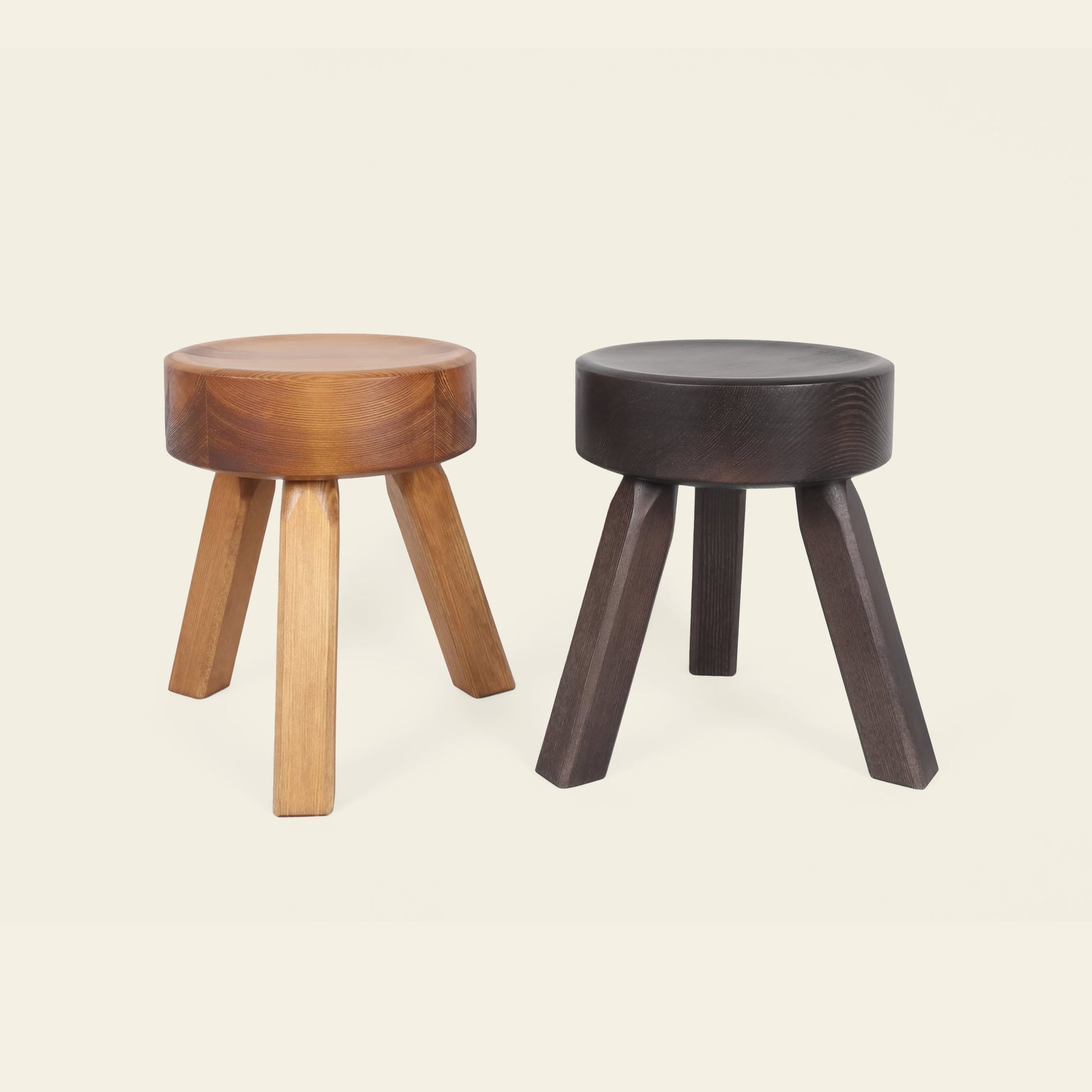 Two FRAMA AML Stools by FRAMA, each with a round seat and three legs, crafted from solid oiled pine in light and dark brown finishes, stand side by side on a plain background to highlight their versatile design.