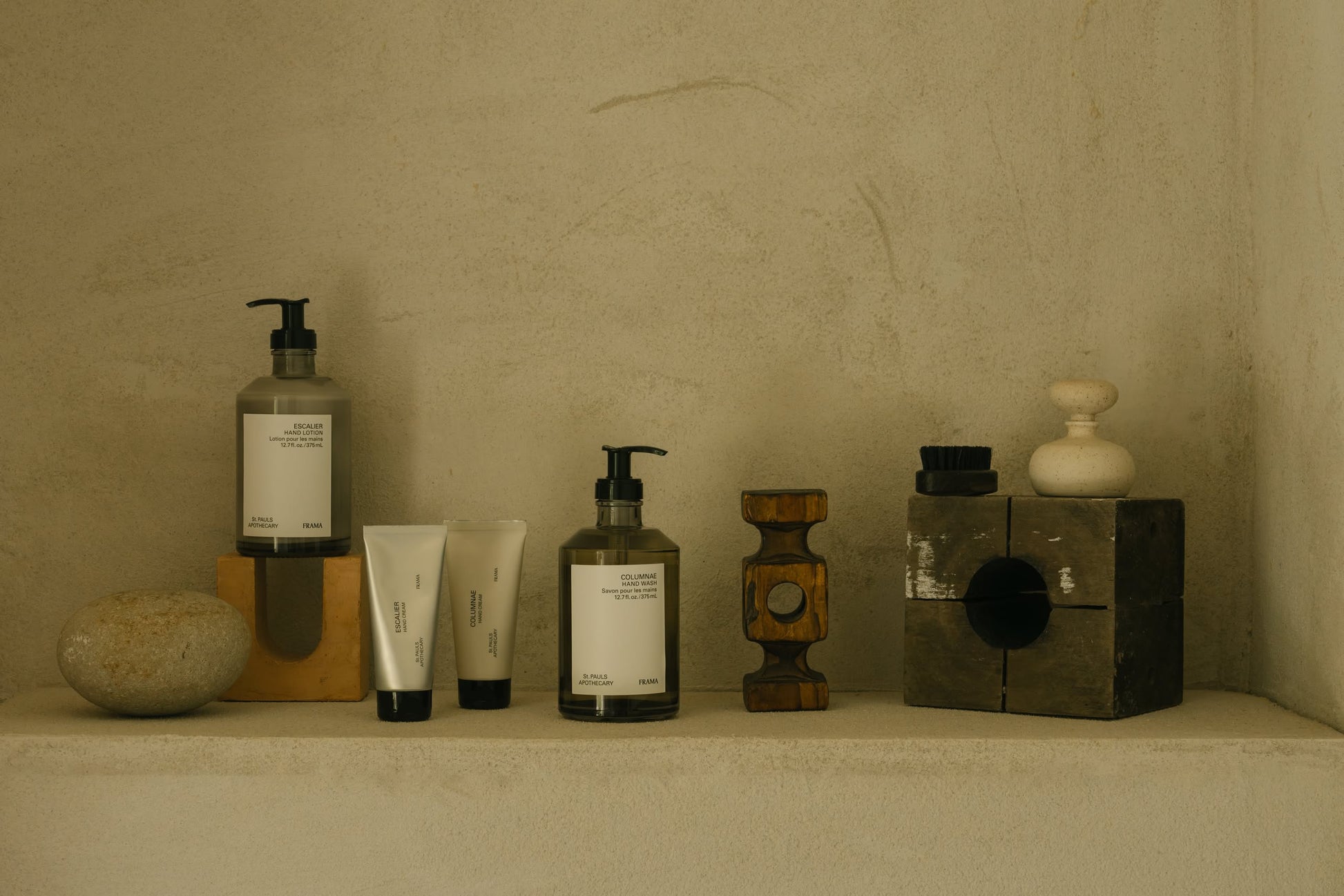 Minimalist display of FRAMA Hand Wash, 375ml, in pump bottles with organic ingredients. Arranged neatly with decorative objects on a beige shelf against a textured wall, featuring a neutral, earthy color palette.