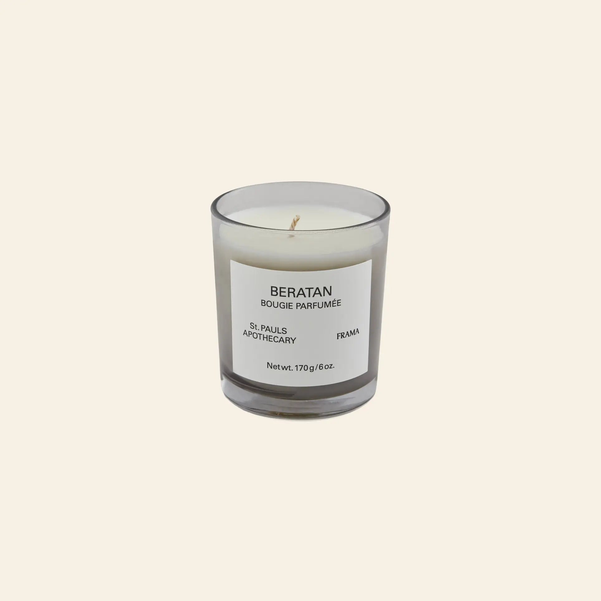 The FRAMA Beratan Scented Candle, 170g, in a clear glass jar with a BERATAN BOUGIE PARFUMÉE label adds warm fragrance and tropical ambiance, showcased on a light beige background.