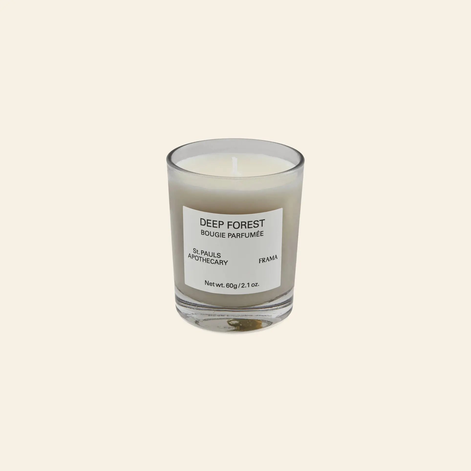 The FRAMA Deep Forest Scented Candle, 60g, in a clear glass holder with a Deep Forest Bougie Parfumée label, evokes the earthy scent of Abies fir woods and is displayed on a plain beige background.