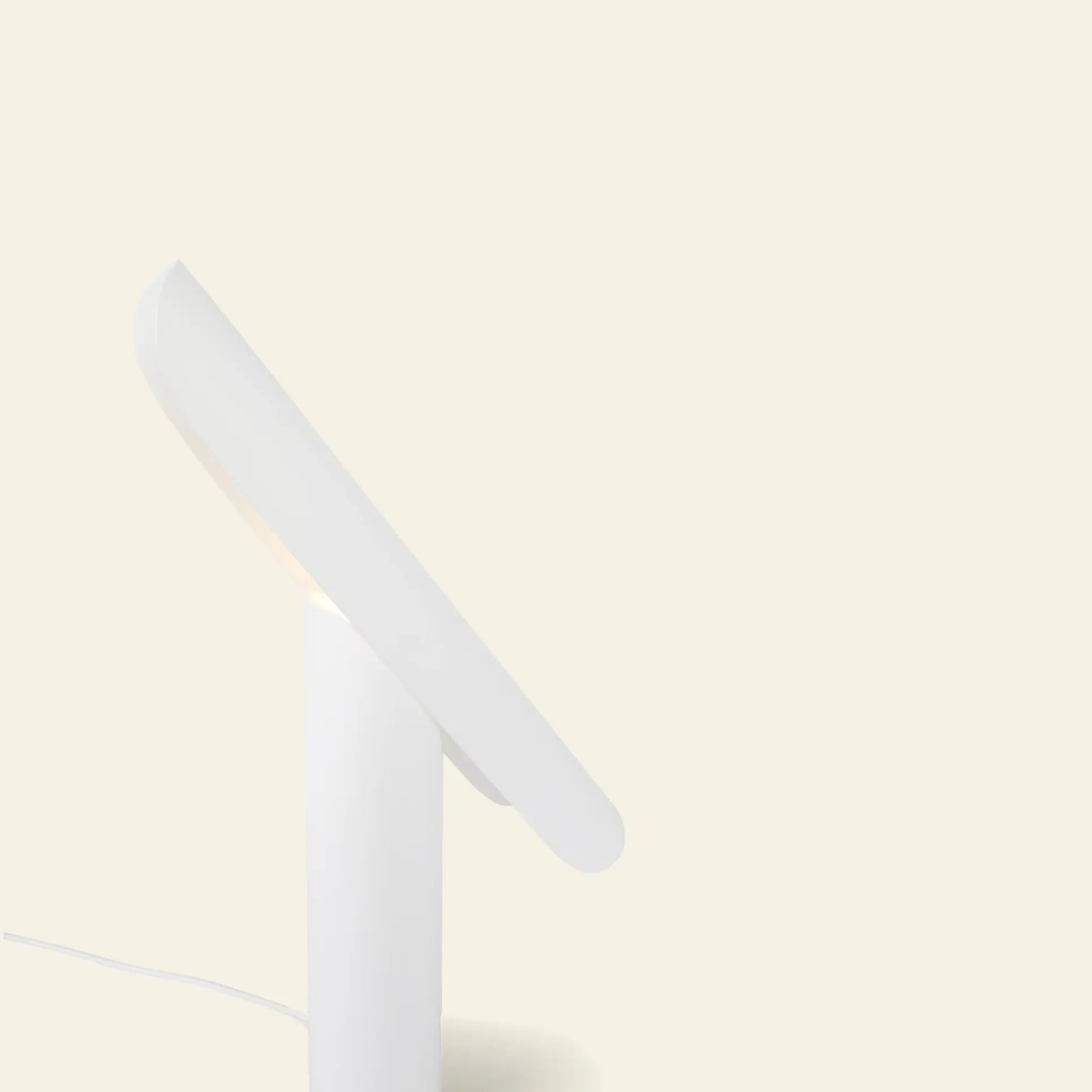 The FRAMA T-Lamp Table Lamp by FRAMA features a minimalist geometric design with an angled flat oval shade, shown against a plain light beige background. The power cord is partially visible on the left side of the image.