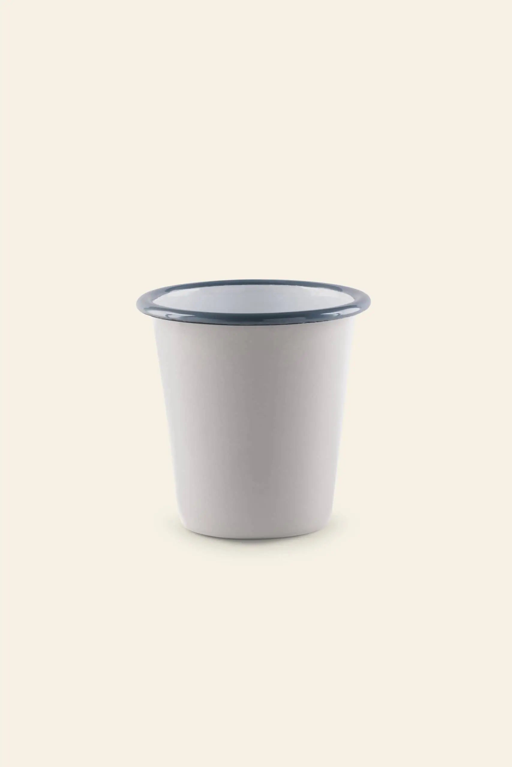 The Falcon Enamelware Tumbler by Falcon Enamelware, a plain white cup with a blue rim set against a light beige background, brings vintage style charm to any setting.