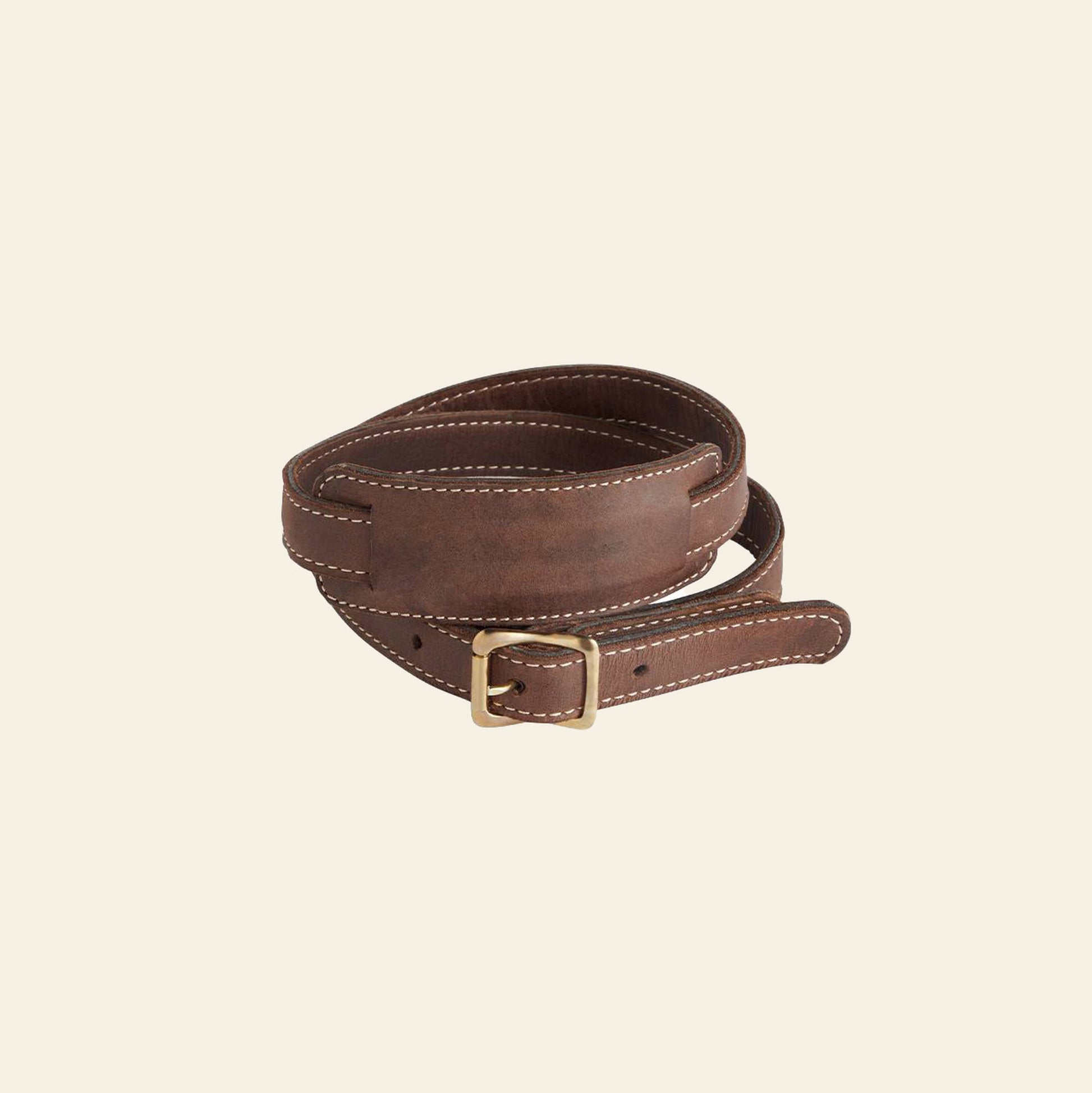 The Fieldbar Drinks Box Sling by Fieldbar, crafted from premium brown leather with white stitching and a rectangular brass buckle, is displayed coiled neatly against a plain light background for a stylish hands-free solution.