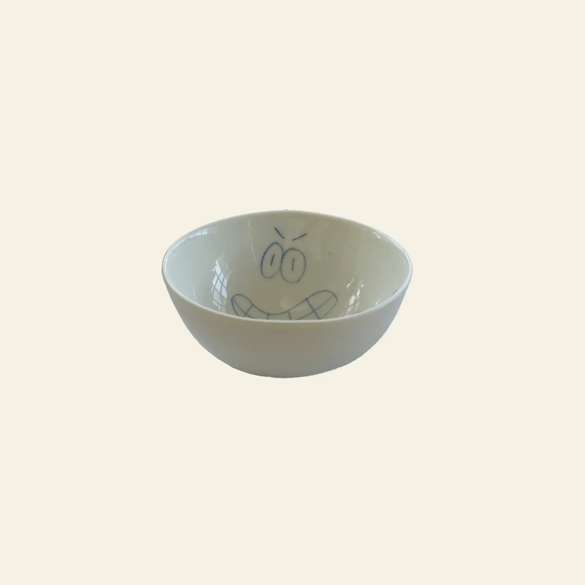The Frizbee Ceramics BBOL S by Frizbee Ceramics is a white ceramic bowl featuring an artisanal, hand-drawn angry cartoon face with furrowed brows and gritted teeth on a plain light background.