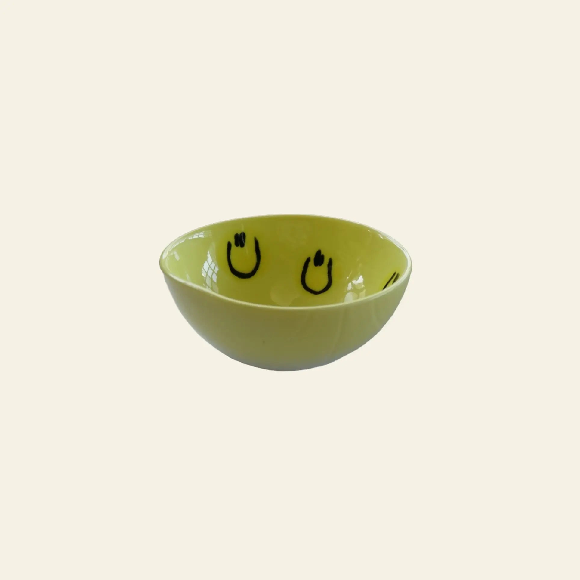 The Frizbee Ceramics BBOL S by Frizbee Ceramics is a small yellow bowl featuring black smiley faces inside, displaying artisanal charm against a simple off-white background.