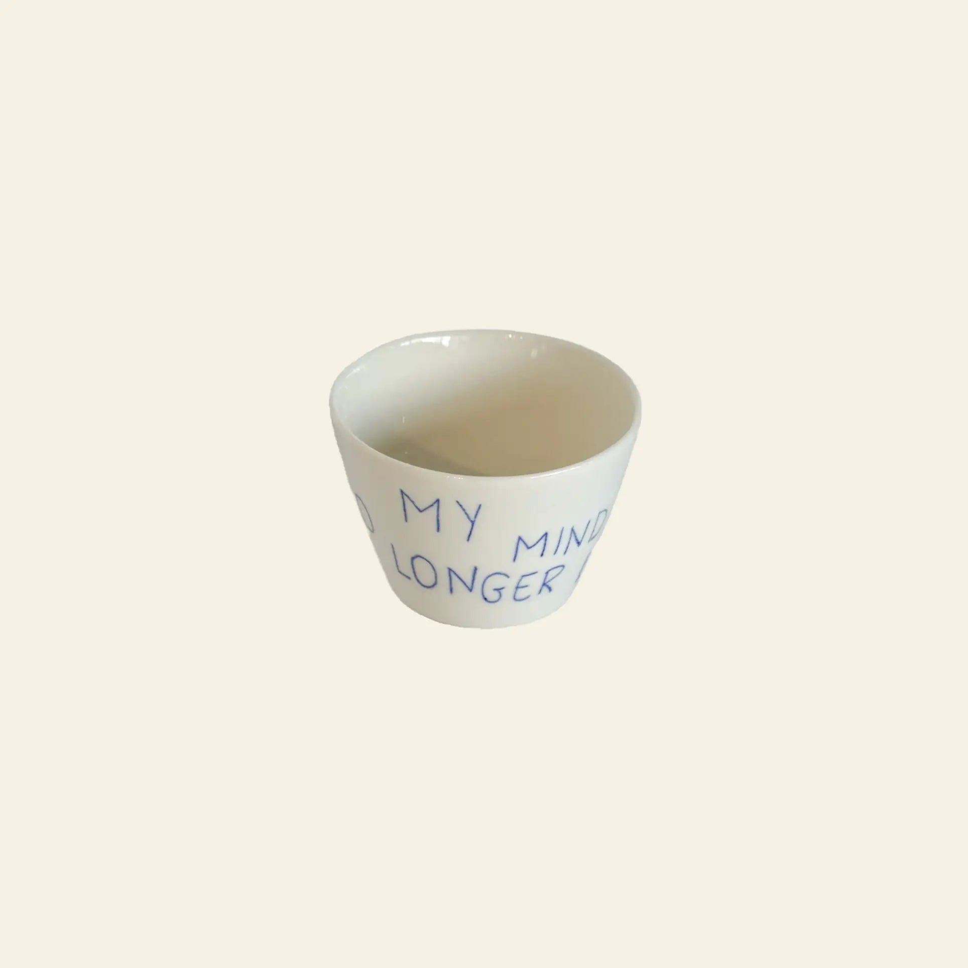 The Frizbee Ceramics Super Cup L by Frizbee Ceramics is a small white ceramic cup featuring blue handwritten text, MY MIND LONGER, on its side, photographed against a plain beige background.