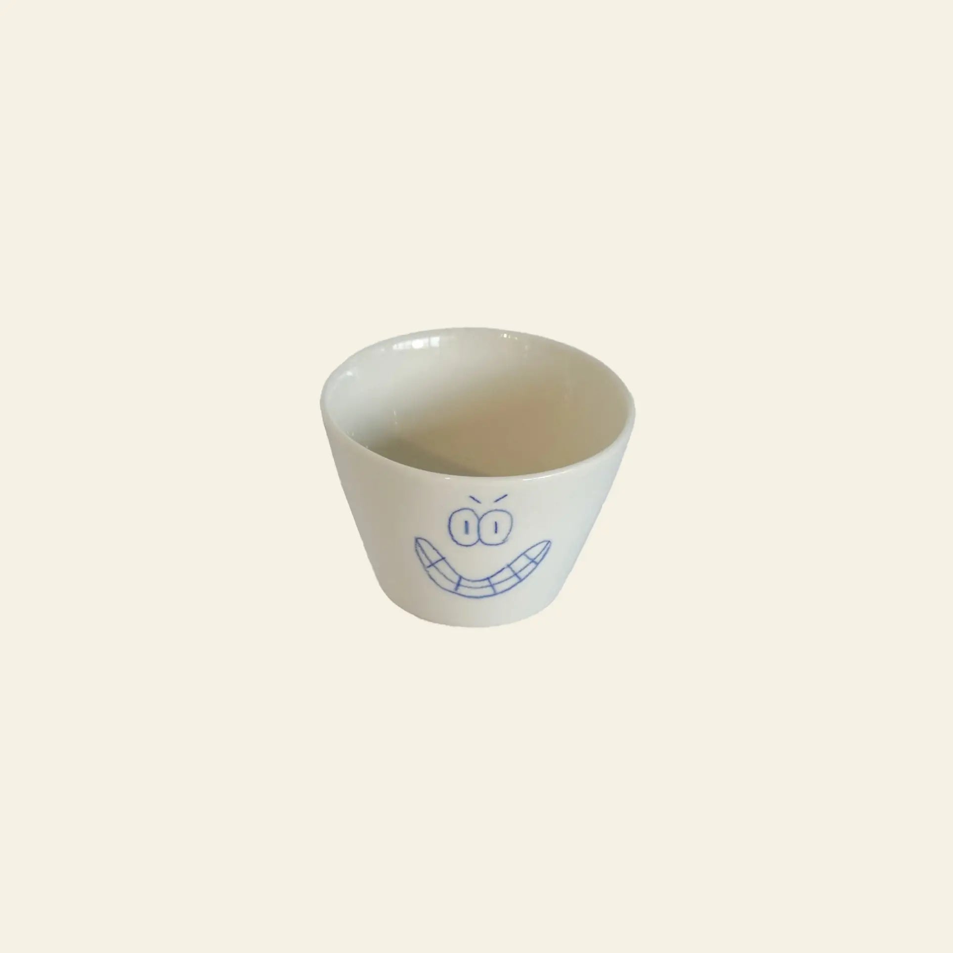 The Frizbee Ceramics Super Cup L by Frizbee Ceramics is a white ceramic cup adorned with a blue cartoon smiley face, making it the perfect artisanal companion for your latte against any background.