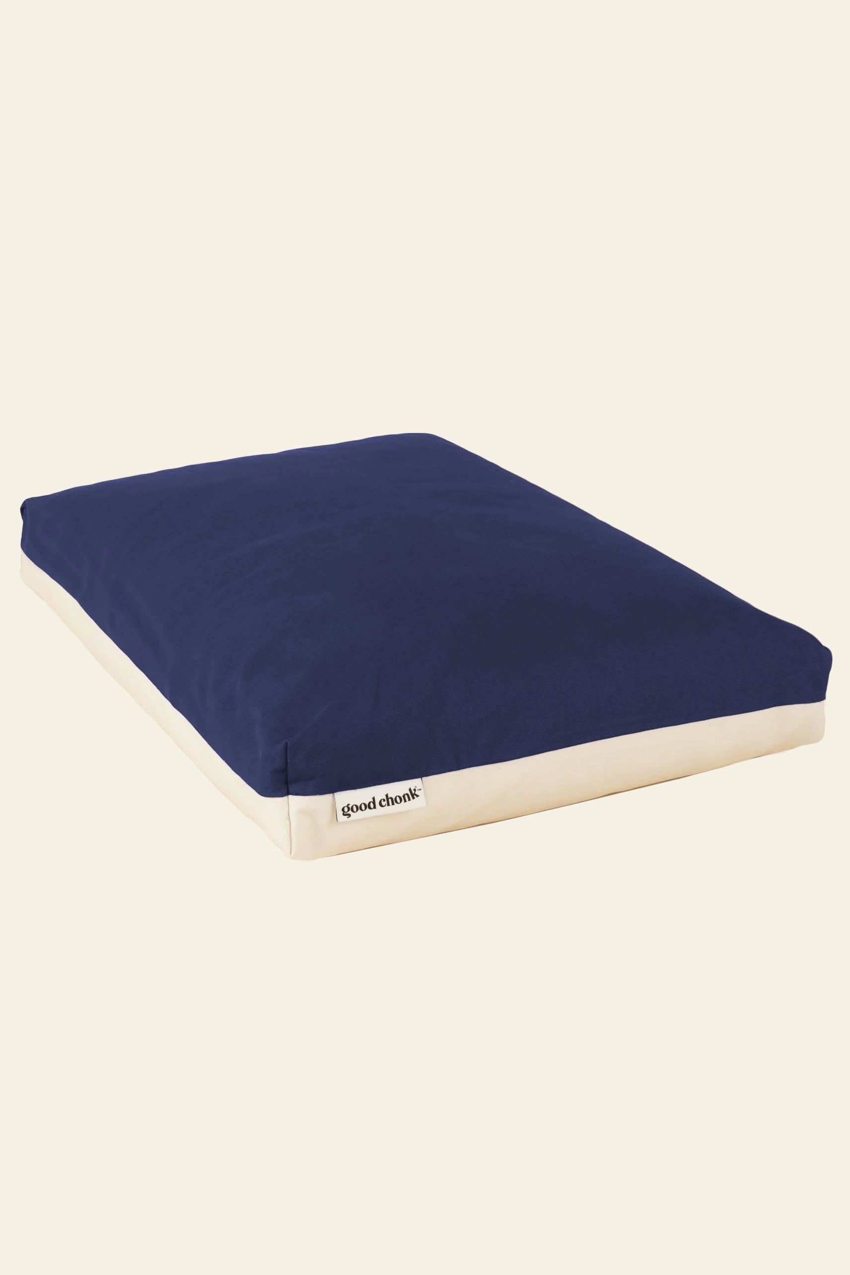 The Good Chonk Cloud Kapok Dog Bed is rectangular with a navy blue top, beige sides, and a front label reading Good Chonk. Made from eco-friendly kapok and a 100% cotton canvas cover, its shown on a plain light background.
