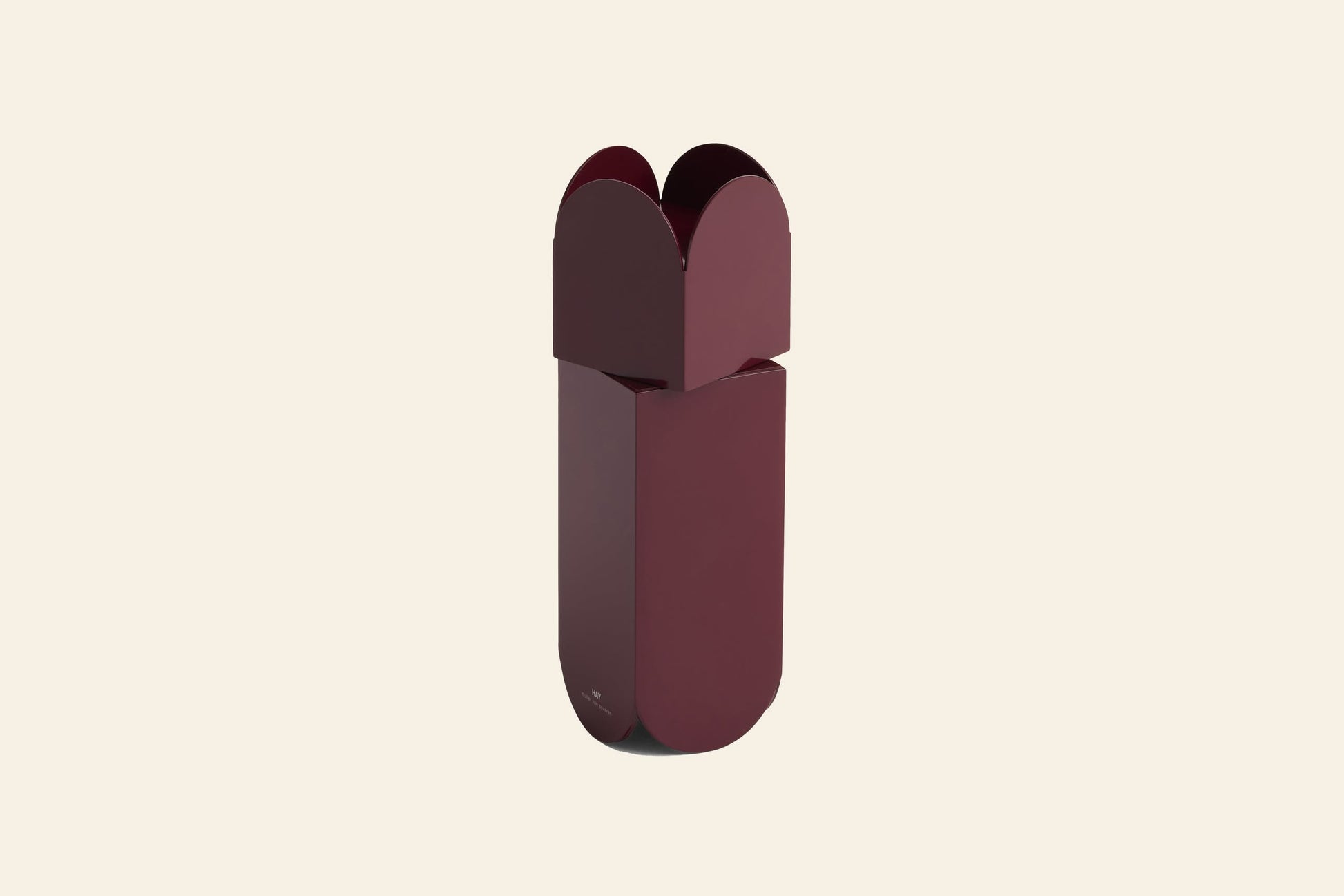 A tall, modern maroon HAY Arcs Salt & Pepper Grinder by HAY features rounded edges and a unique clover-shaped top inspired by sleek stainless steel grinders, set against a plain cream background.