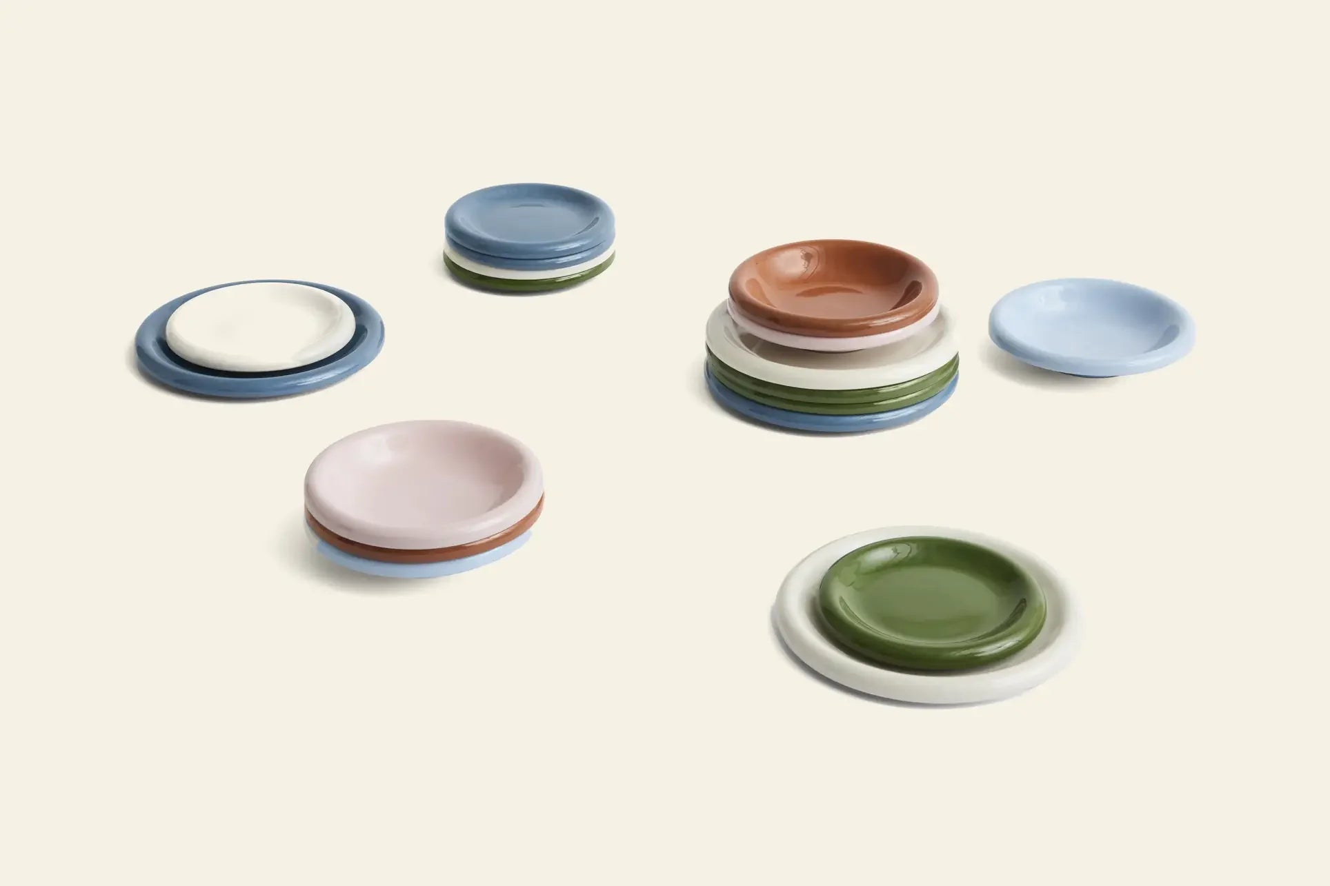 Small ceramic plates in assorted colors are displayed on a beige background. Designed by a Portuguese designer, these round plates pair beautifully with the HAY Barro Bowl, Set of 2 for a simple, modern look.