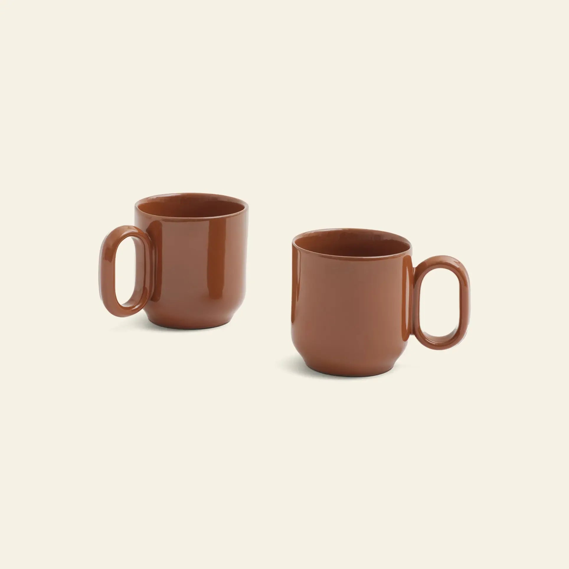Two HAY Barro Cups in brown terracotta, designed by Rui Pereira, feature large handles and rest separately on a beige background. The simple ceramic set by HAY highlights minimalist design and elegant presentation.