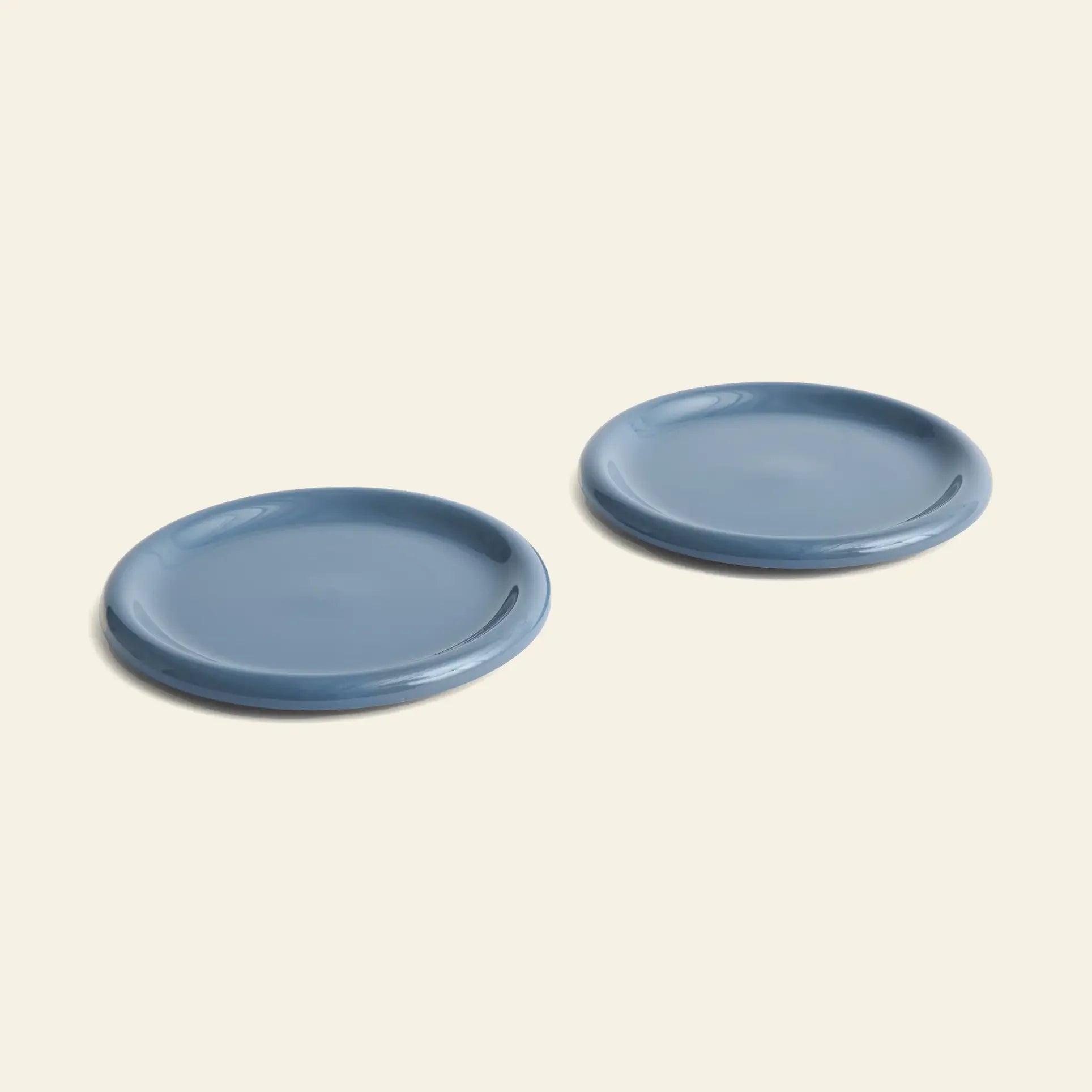 Two blue HAY Barro Plate 24cm ceramic plates (set of 2) are displayed side by side on a light beige background, featuring a simple, smooth design with slightly raised edges.