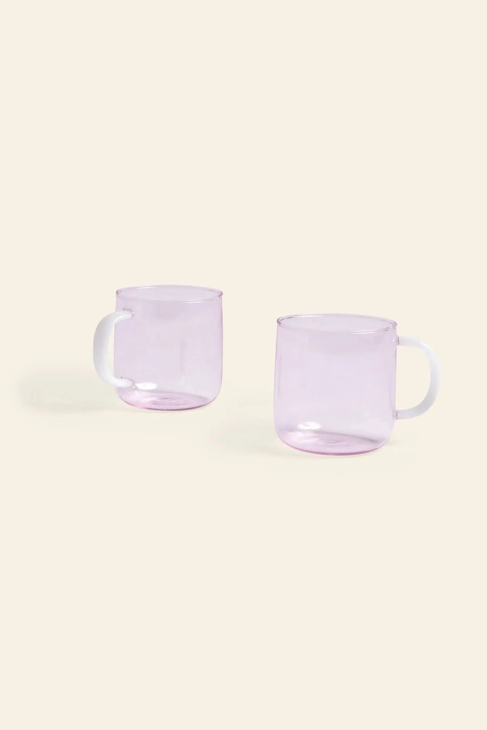 Two translucent light purple HAY Borosilicate Mug, Set of 2 by HAY with white handles sit on a plain beige background. Lightweight and heat-resistant, these modern mugs are perfect for any setting.