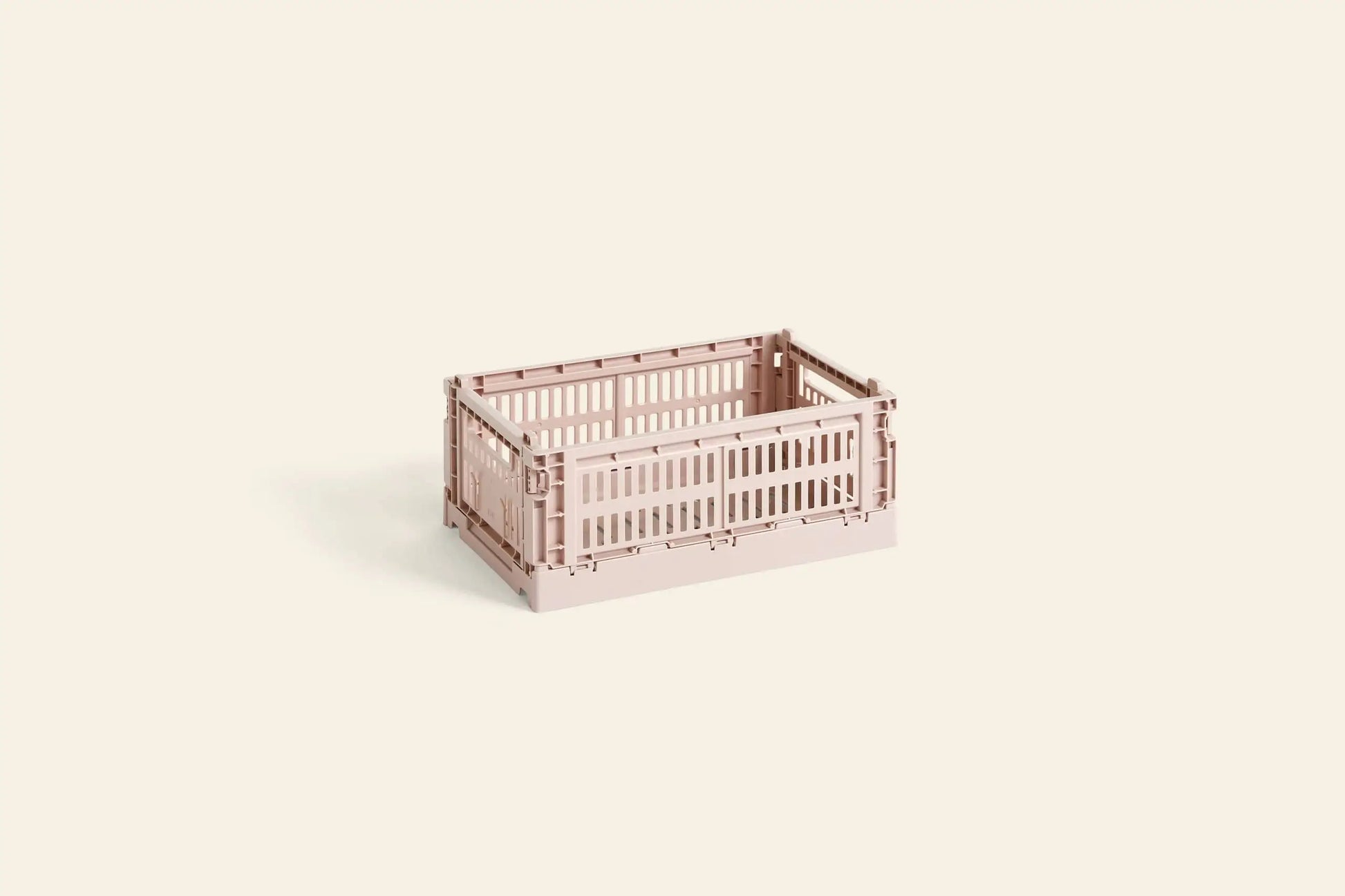 A HAY Colour Crate Small by HAY in light pink sits on a plain beige background. This collapsible, stackable crate with slatted sides provides a colorful storage solution for organizing your space.