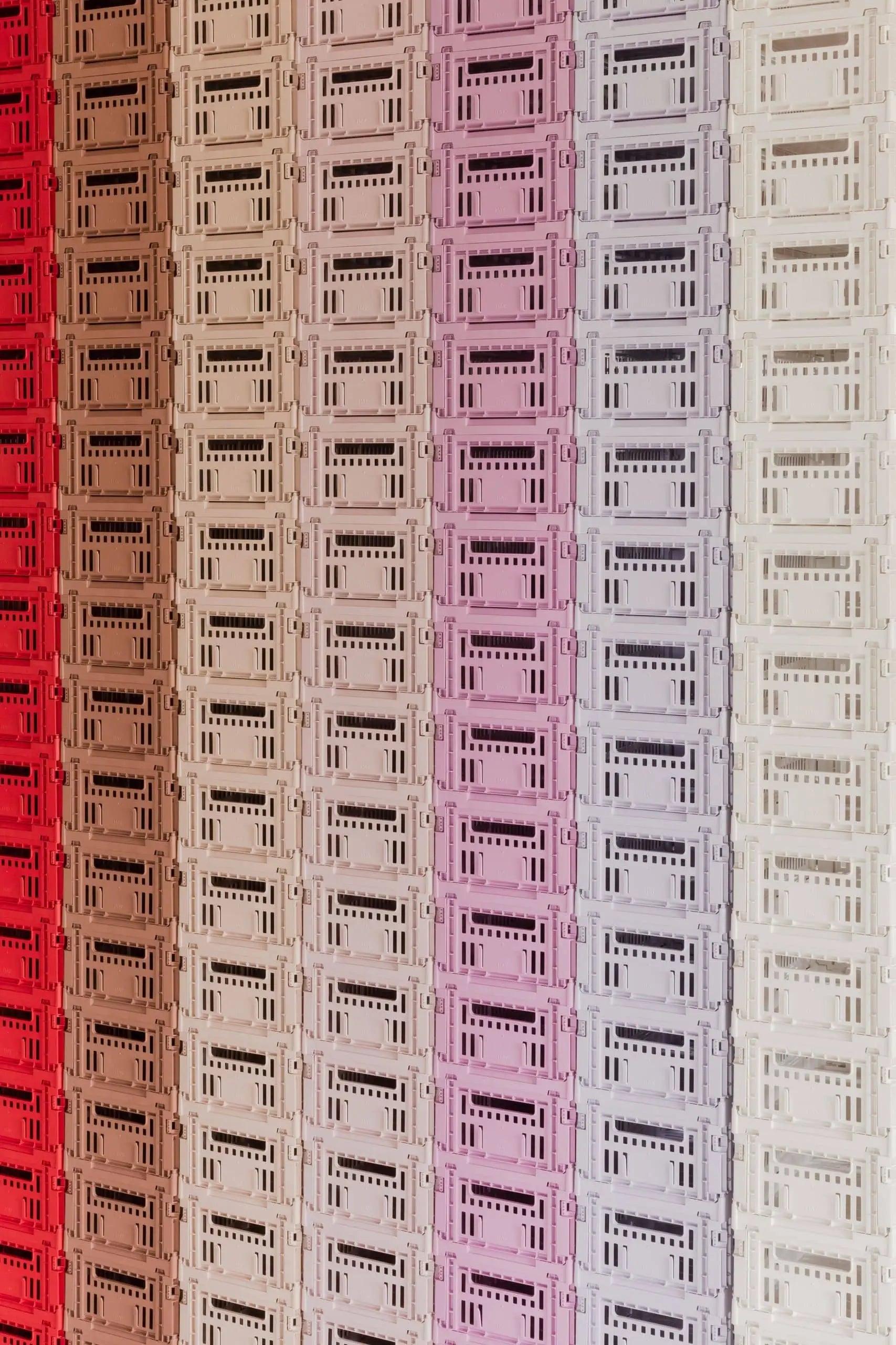 A wall of stacked HAY Colour Crate Small boxes by HAY, arranged in columns, creates a vibrant storage solution with colors transitioning gradually from red on the left to white on the right.