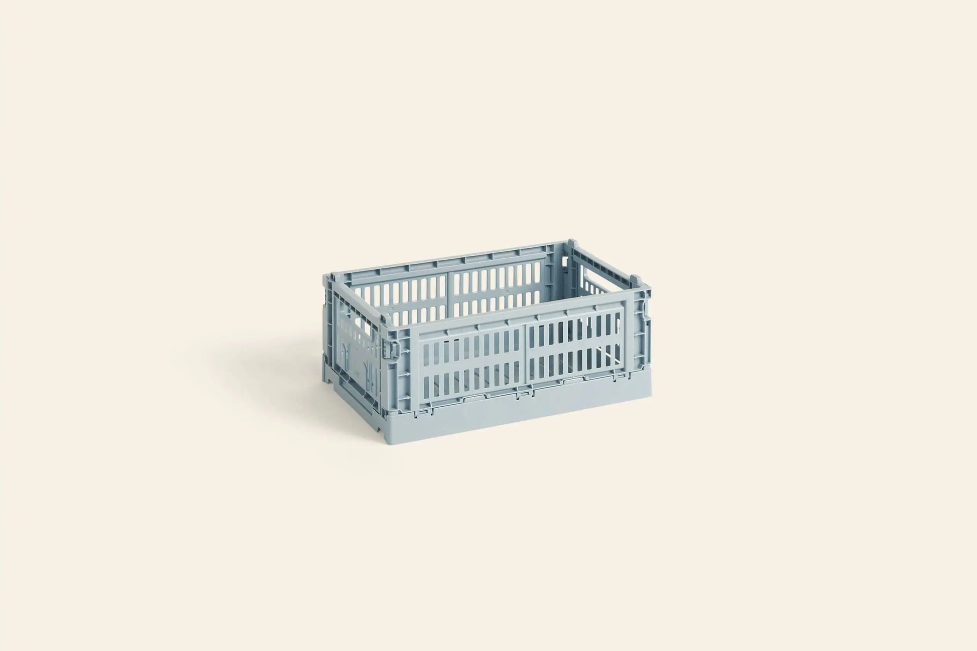 A HAY Colour Crate Small by HAY, featuring slatted sides and folded corners in light blue, sits on a plain light beige background—an ideal colorful storage solution for an organized space.