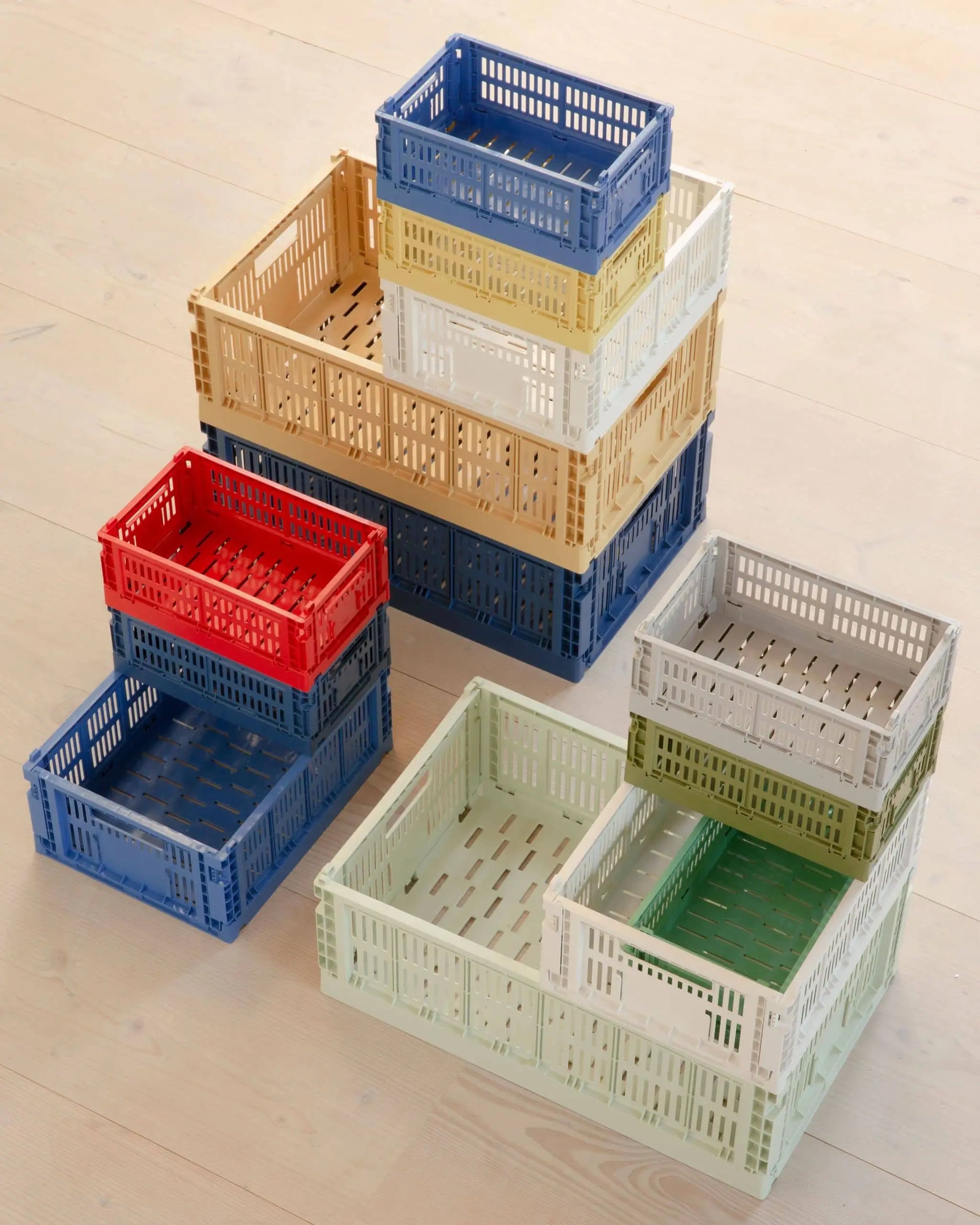 Several HAY Colour Crate Small storage crates by HAY in blue, red, yellow, beige, green, and white are stacked on a light wood floor—an ideal colorful storage solution for an organized living space.