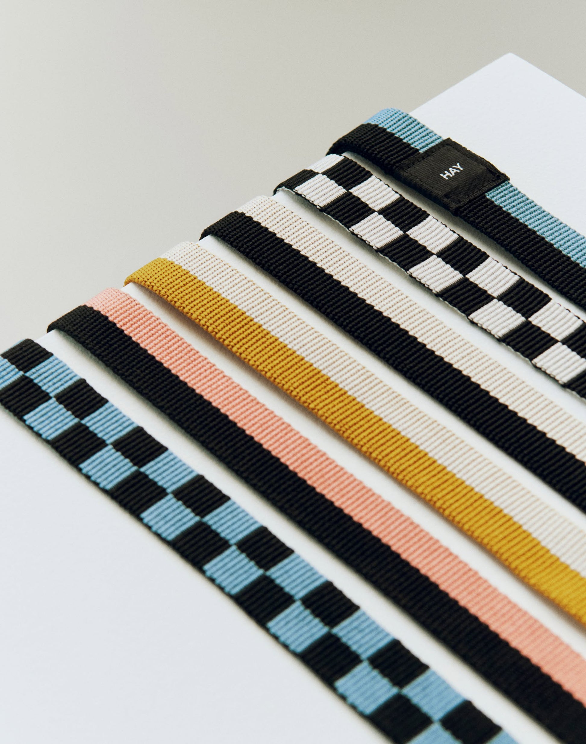 Five HAY Dogs Leash Flat Check straps by HAY, crafted from recycled polyester, showcase blue/black checks, pink/black stripes, yellow/white stripes, and black/white checks—arranged parallel on a white surface.