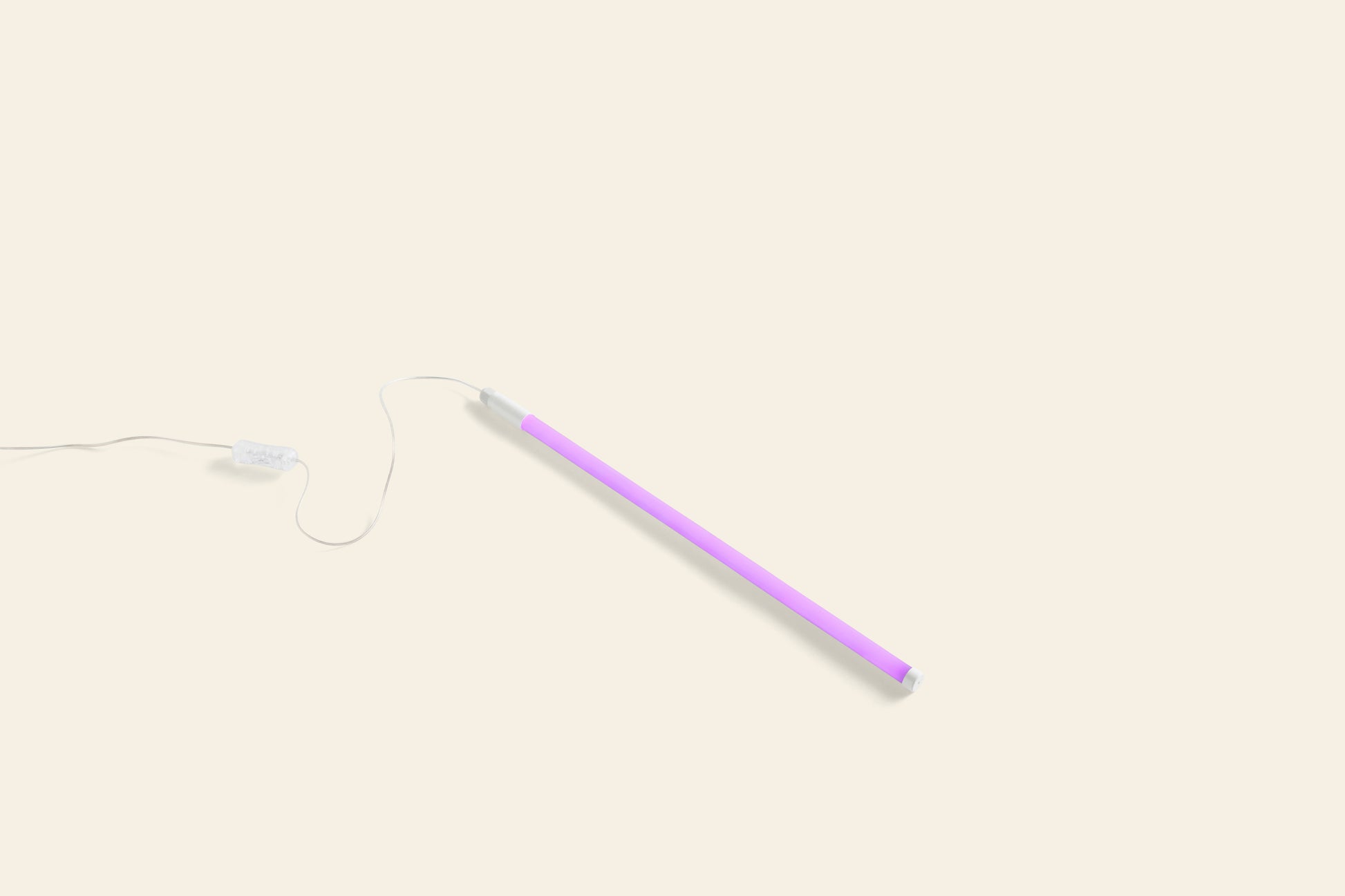 The HAY Neon Tube LED Slim 50cm by HAY, in glowing purple with a connected power cord, lies on a light beige background, casting vibrant colorful light to create an energetic ambiance.