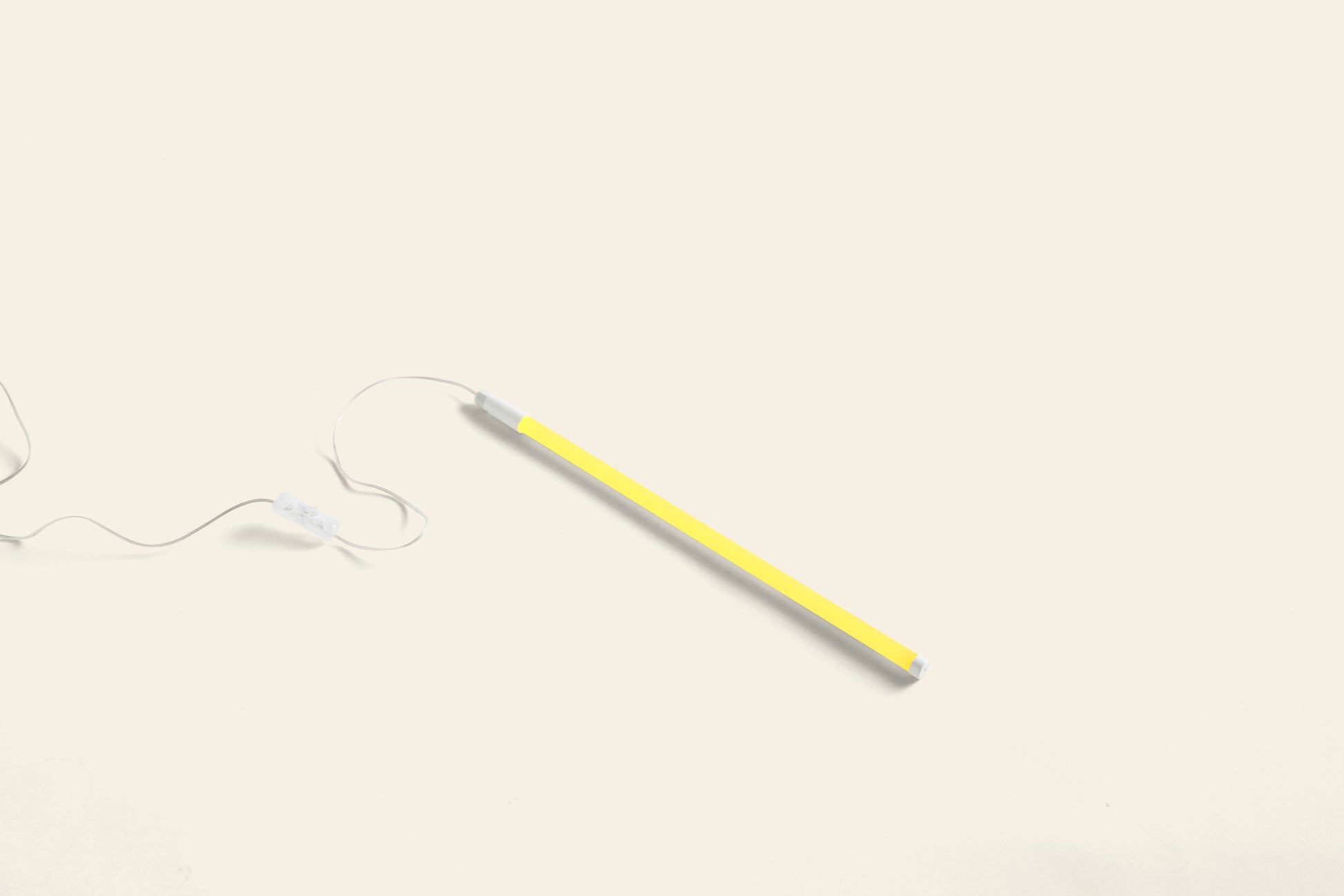 The HAY Neon Tube LED Slim 50cm by HAY, a yellow stick-shaped light with white tips, hangs from a thin white cord that extends to the left against a plain, light background.