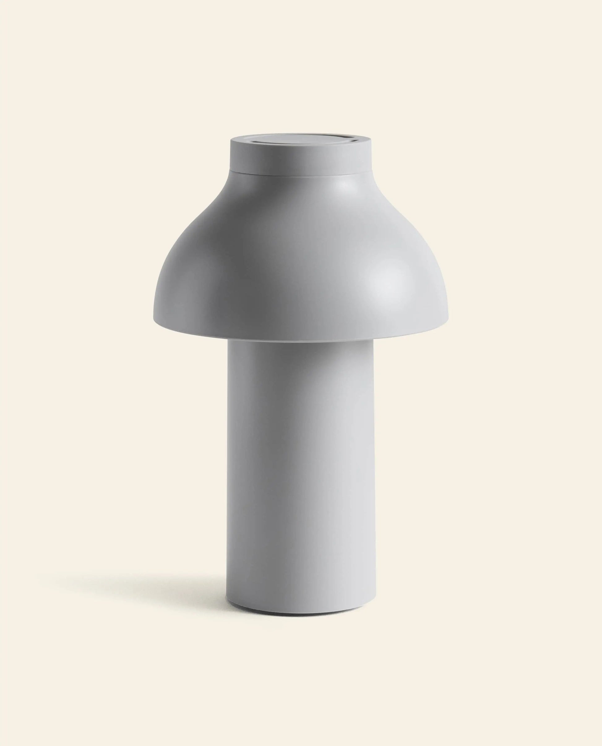 The HAY PC Portable Lamp by HAY features a minimalist, modern design with a cylindrical base and a wide dome shade in matte light gray, subtly channeling Art Deco style against an off-white background.