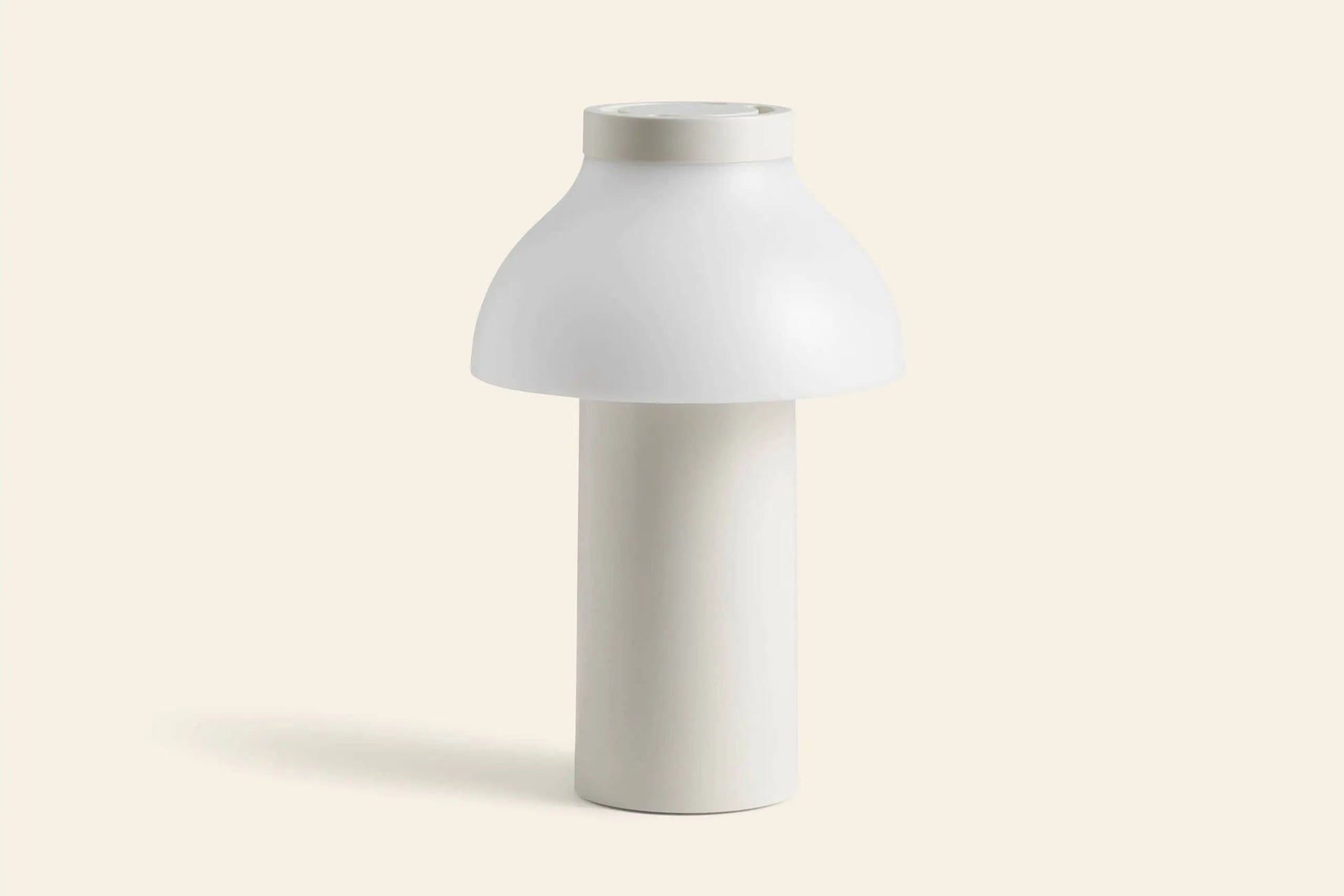 The HAY PC Portable Lamp by HAY features a modern white design with a cylindrical base and dome-shaped shade, inspired by Art Deco, shown against a plain light beige background.