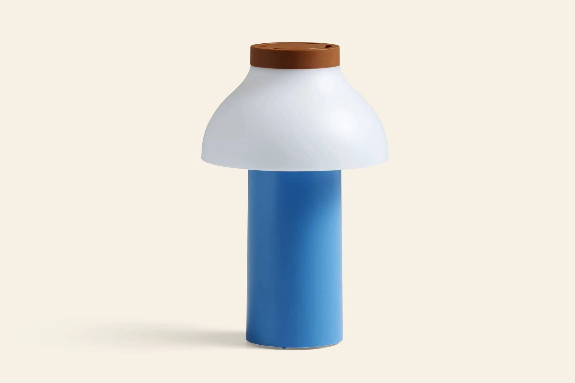 The HAY PC Portable Lamp by HAY features a modern Art Deco design with a cylindrical blue base, wide white dome-shaped shade, and brown circular top, set against a plain light beige background.